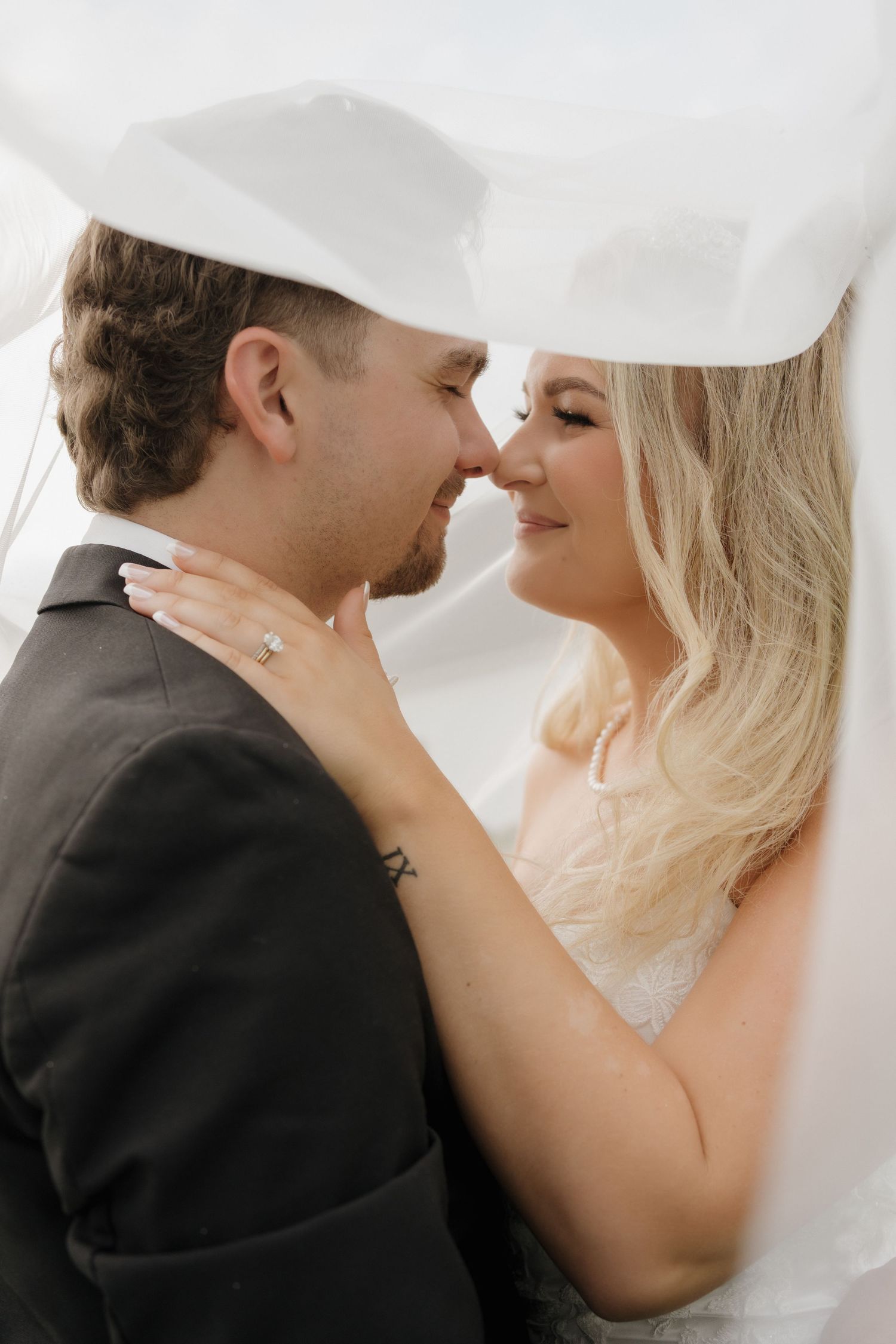 A romantic wedding couple shares an intimate moment under a delicate white veil.