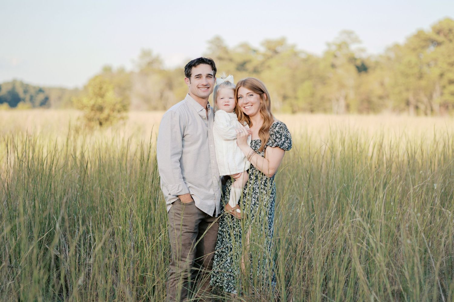 A family poses together in a sunlit meadow with tall grass during golden hour at sunset.