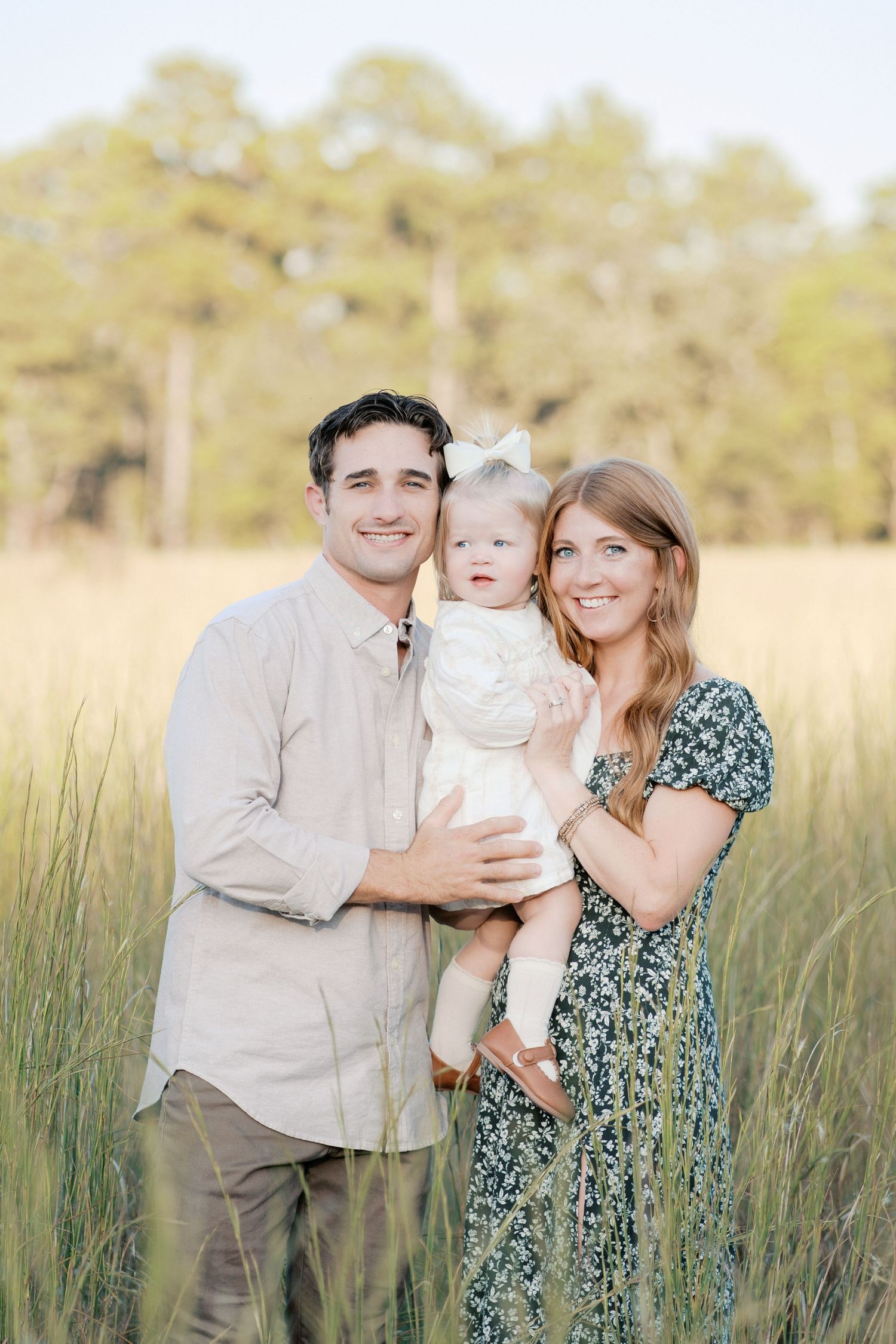 A loving family poses together in a sunlit field of tall grass during golden hour.