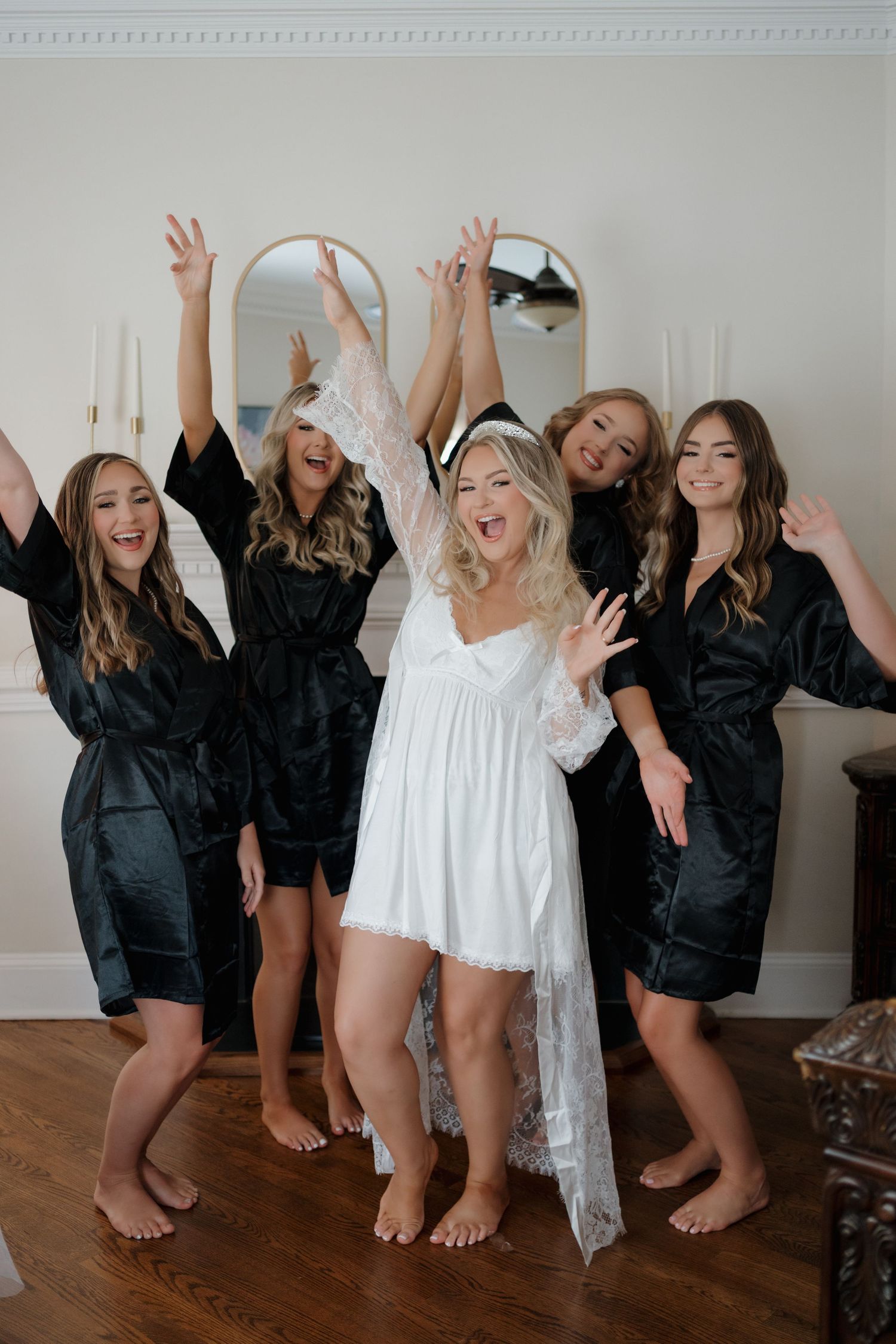 Bridal party wearing black silk robes celebrates with bride in white during wedding day preparations.