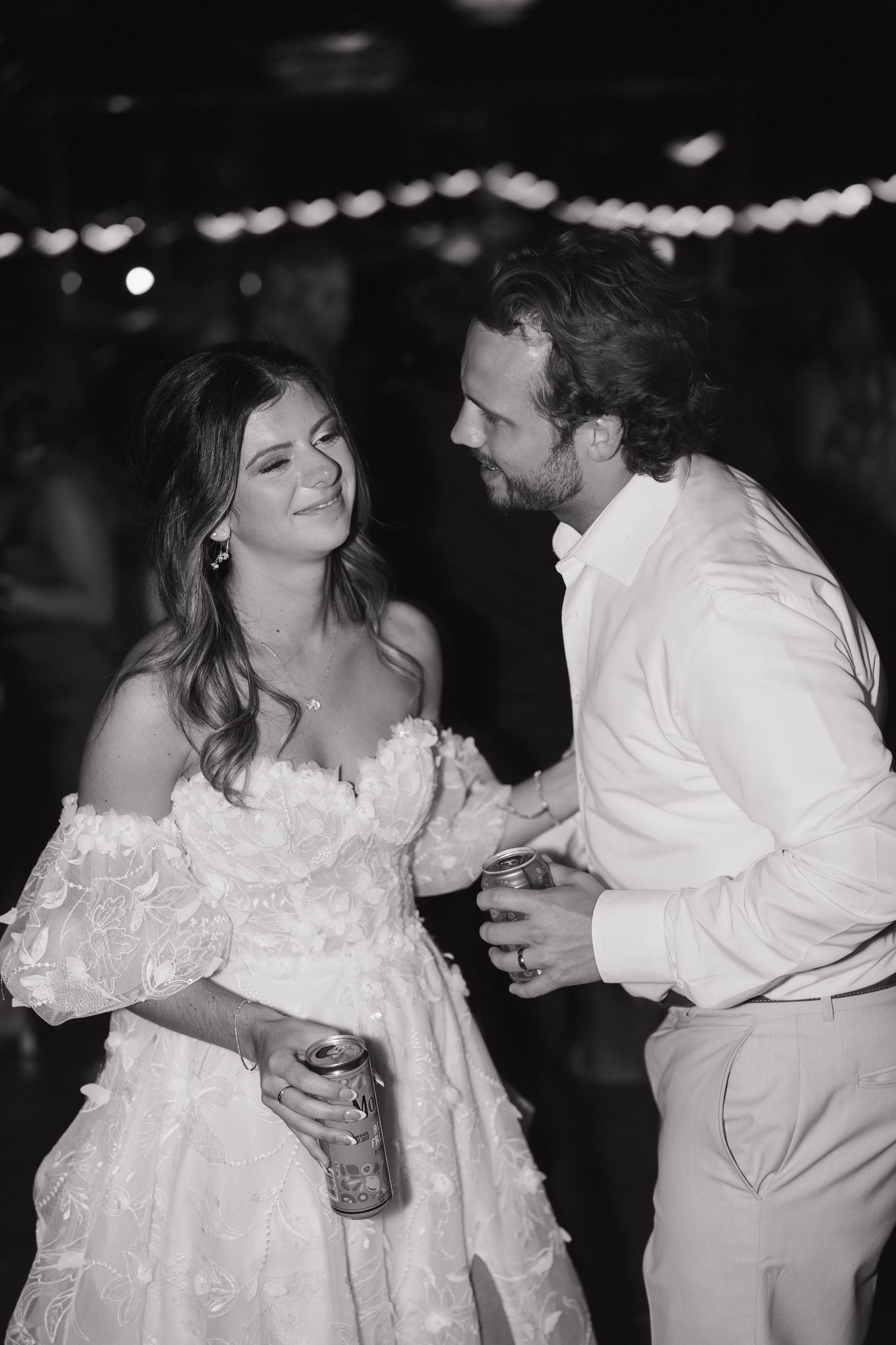 A black and white photo of a couple dancing intimately at their wedding reception under string lights.