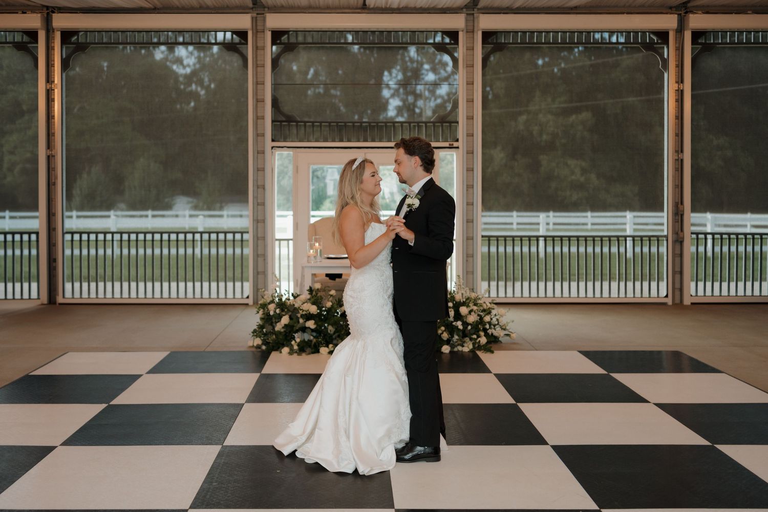 A couple shares a romantic moment on a vintage checkerboard floor porch with floral arrangements in the background.