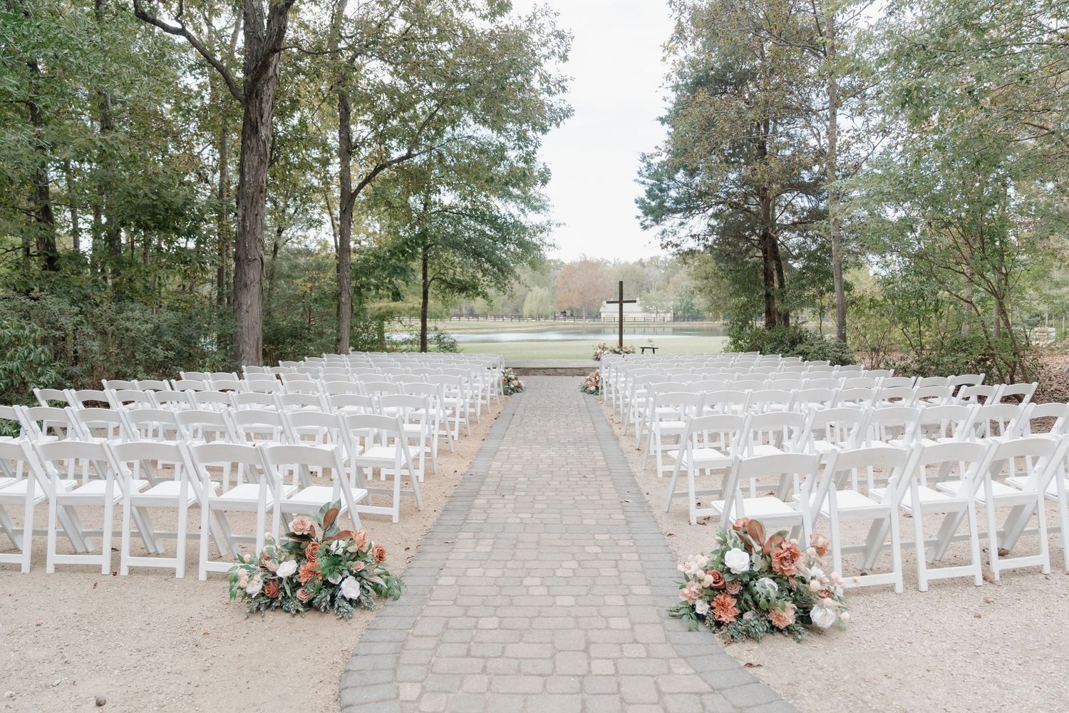 Panoramic view of white chairs set up for an outdoor wedding ceremony with floral arrangements along the stone pathway.