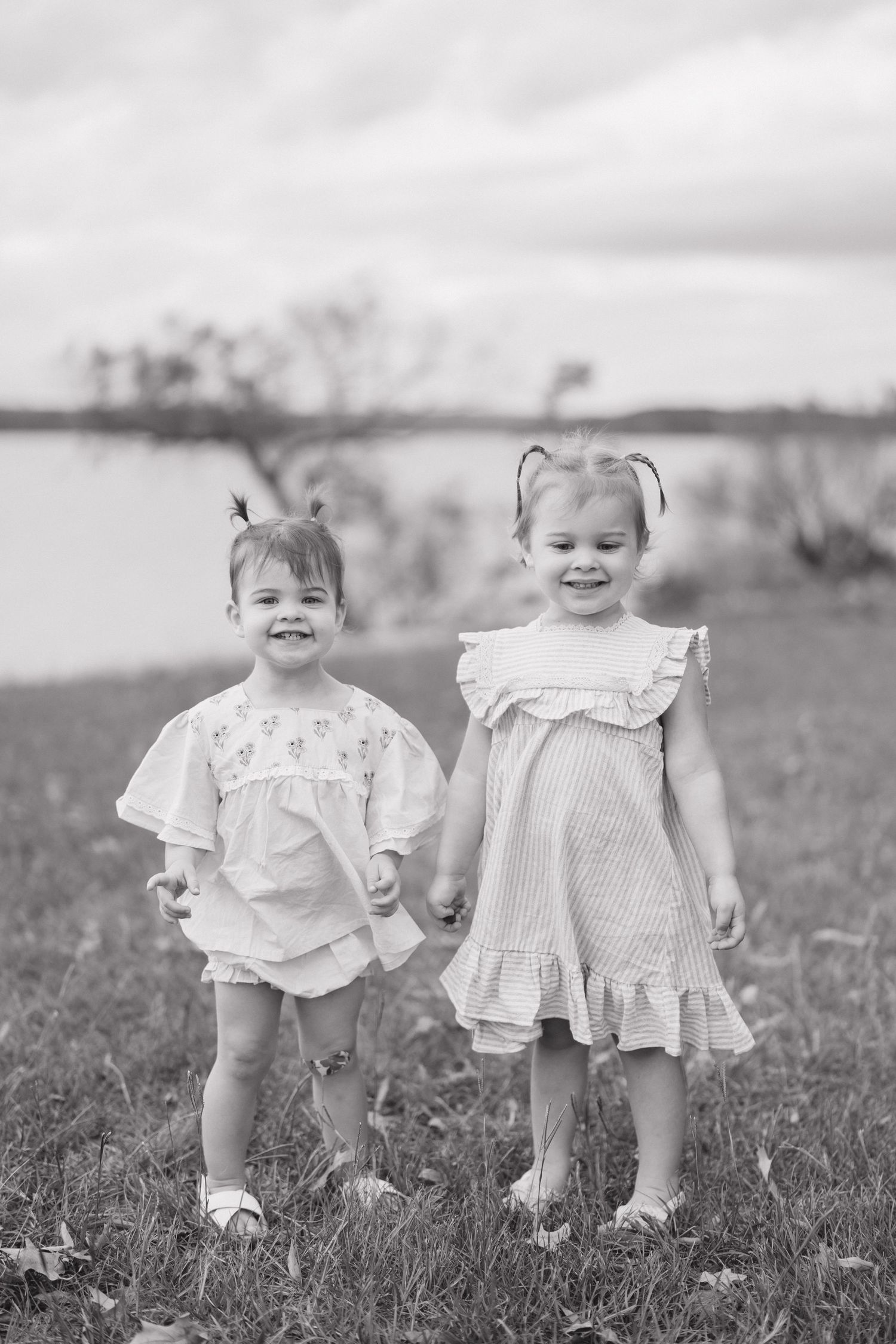 A series of black and white photographs showing two small children in white dresses standing together in a grassy field.