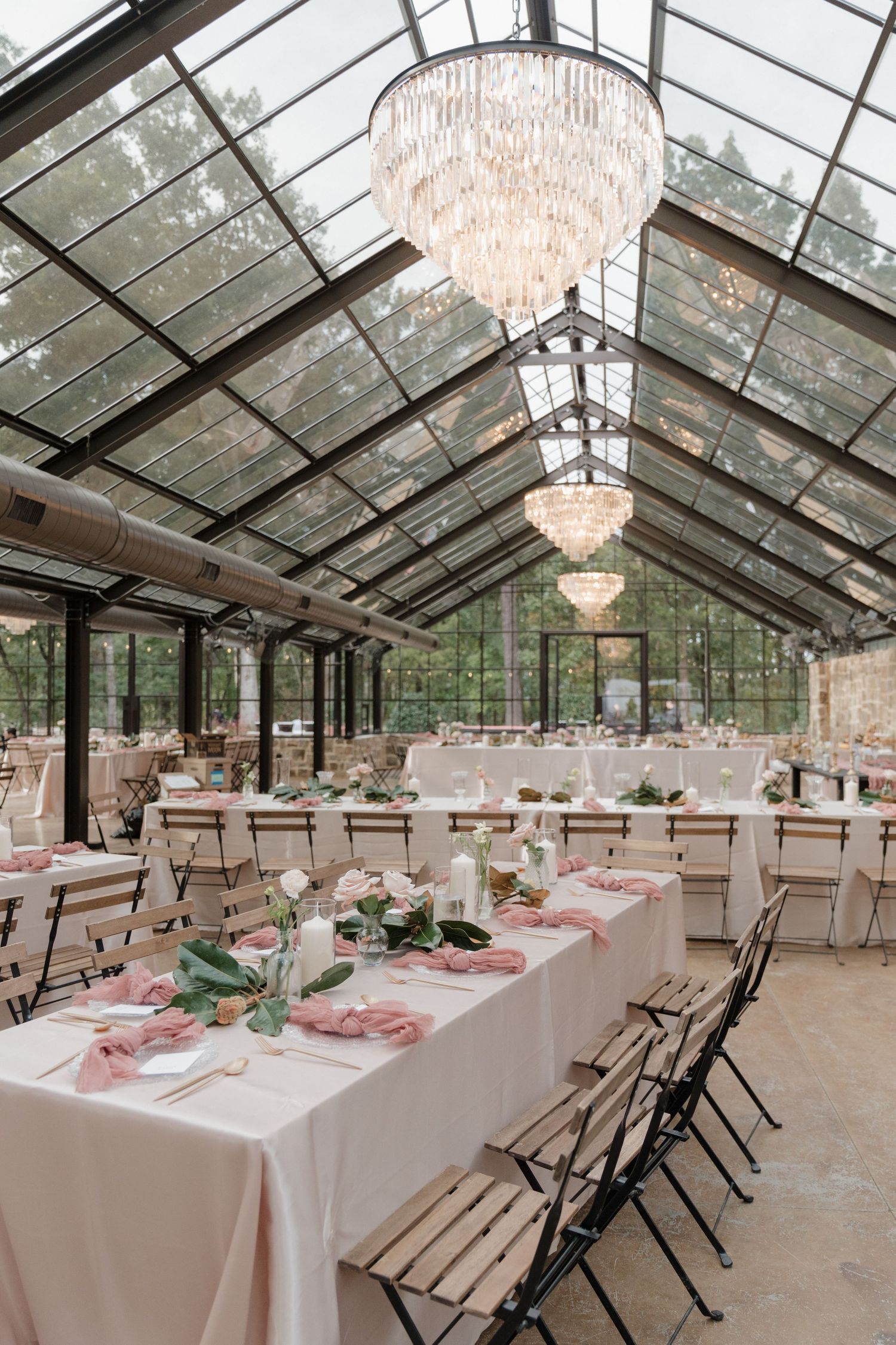 An elegant wedding reception venue with glass ceiling, crystal chandeliers and tables set with pink accents.
