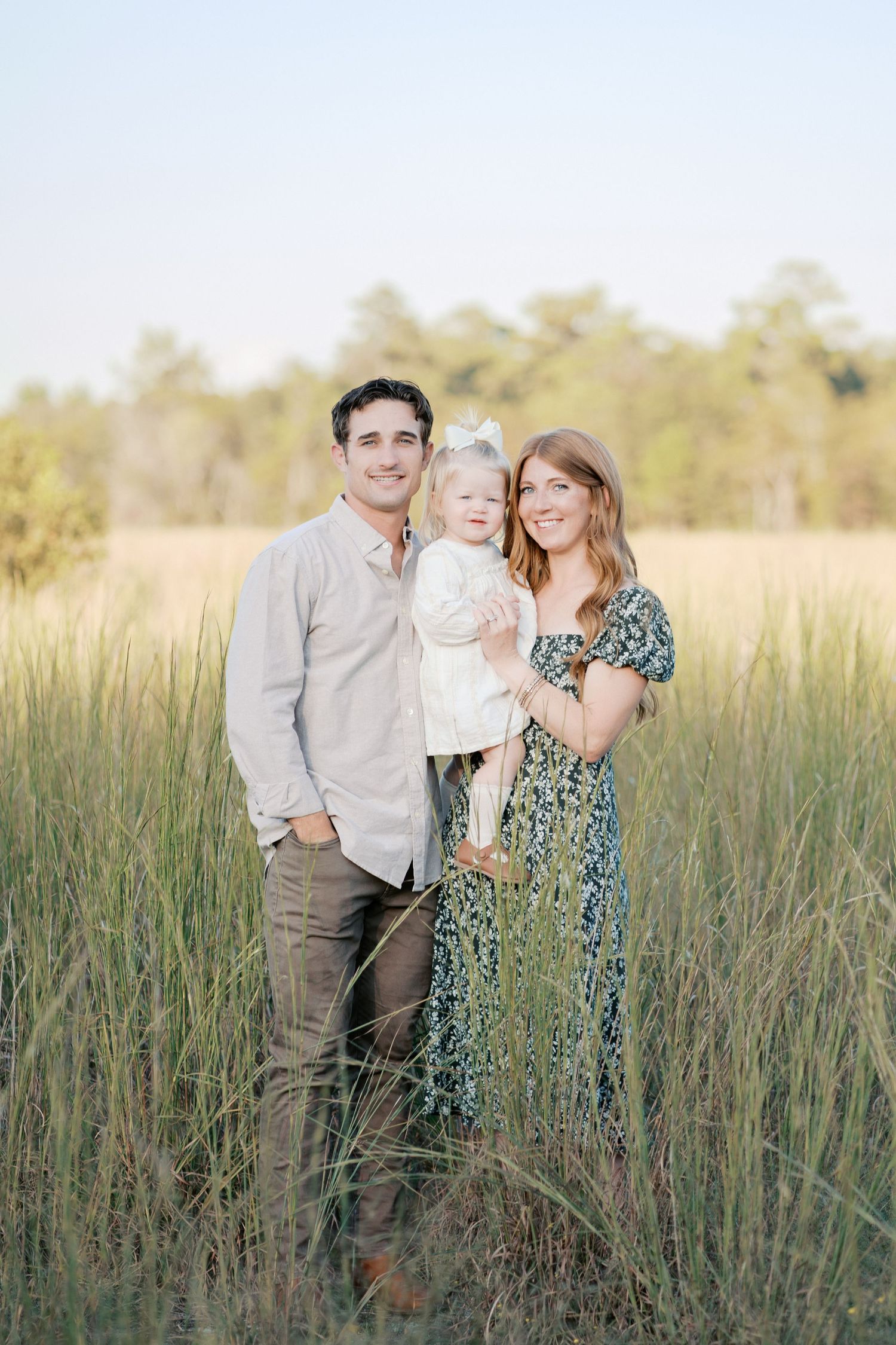 A family poses together in tall grass during a sunset outdoor photoshoot.