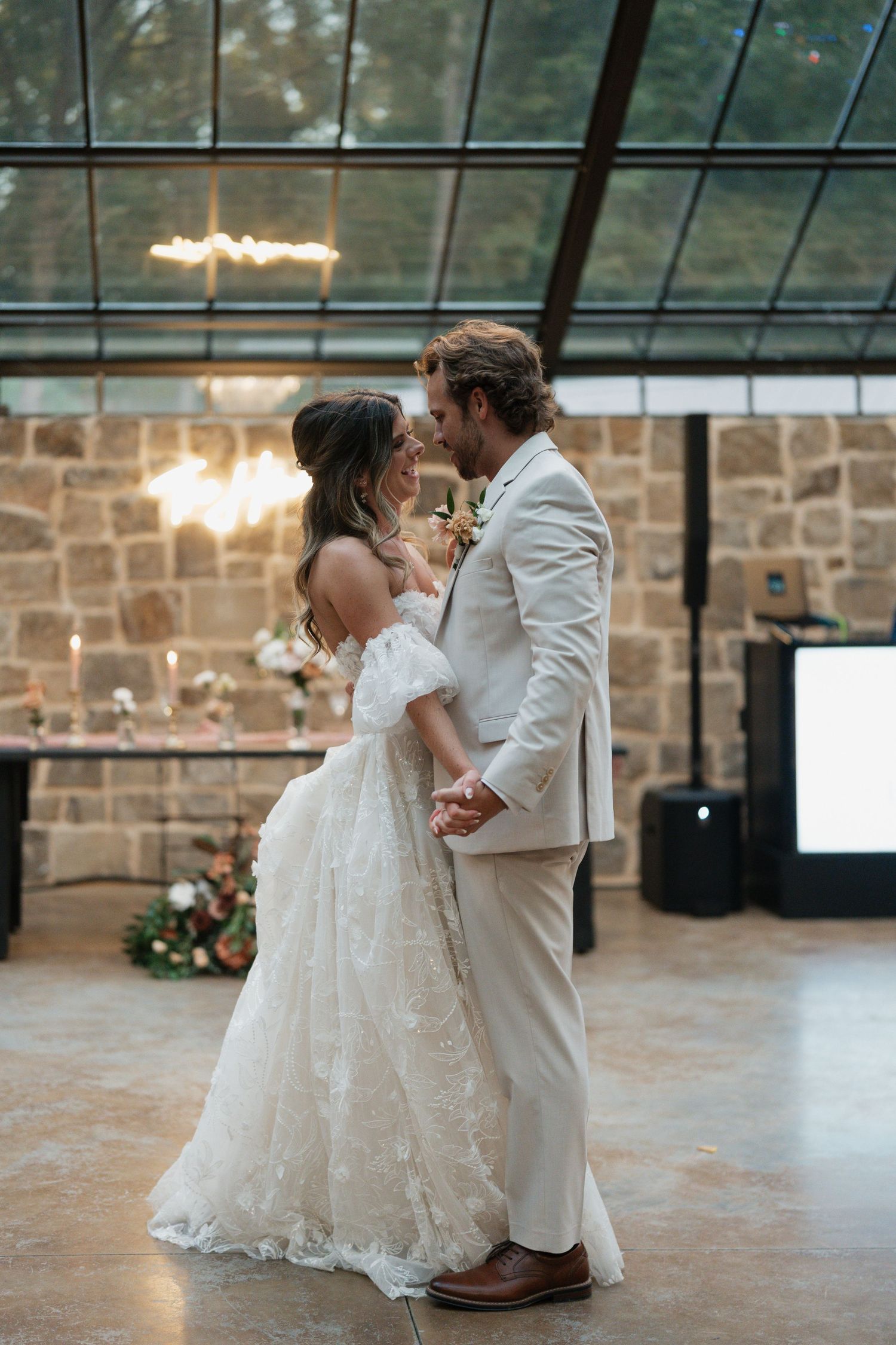 First dance moment captured in stone venue with arched glass ceiling and ambient lighting.