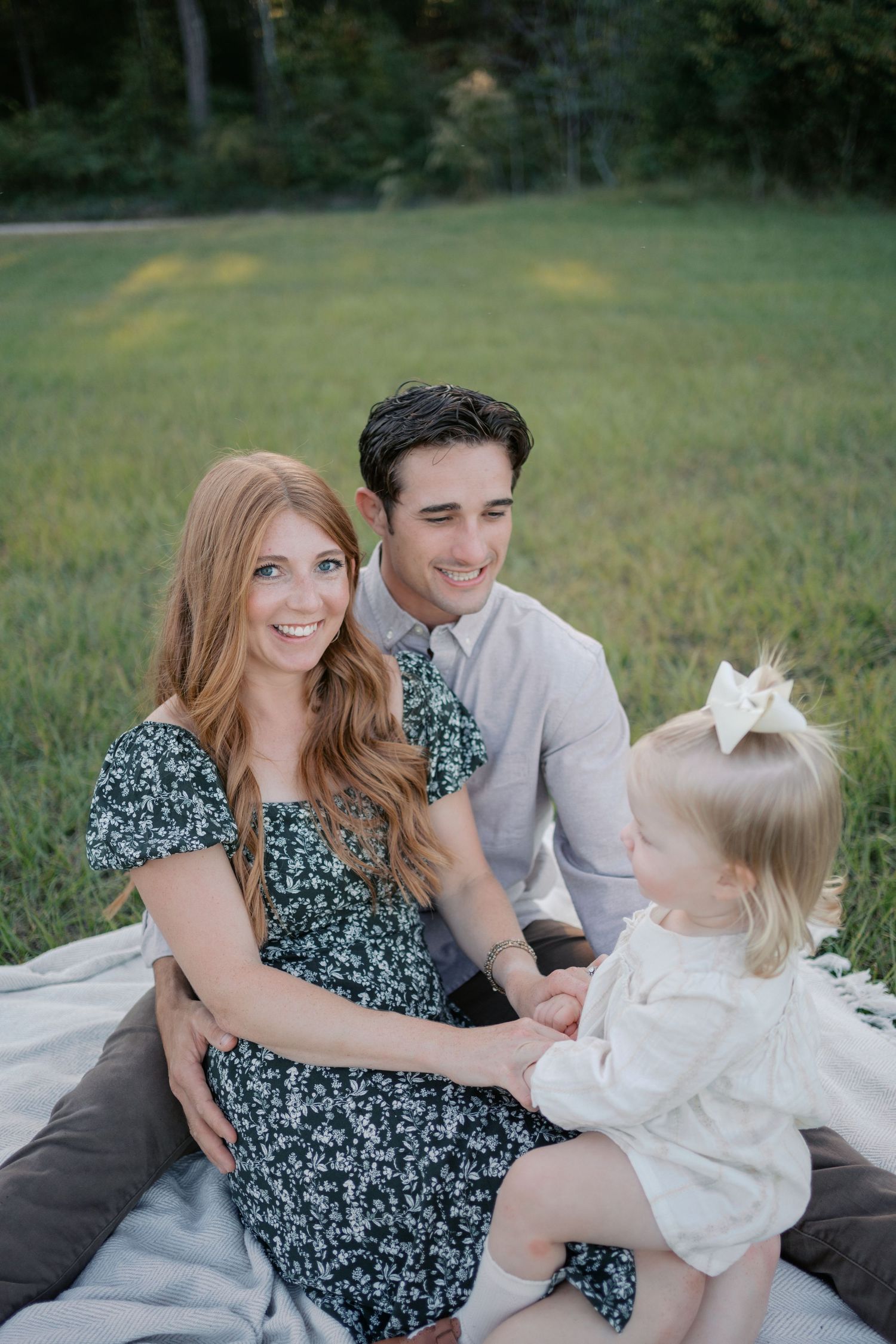 A family sits together on a blanket in a sunlit meadow for a casual outdoor photoshoot.