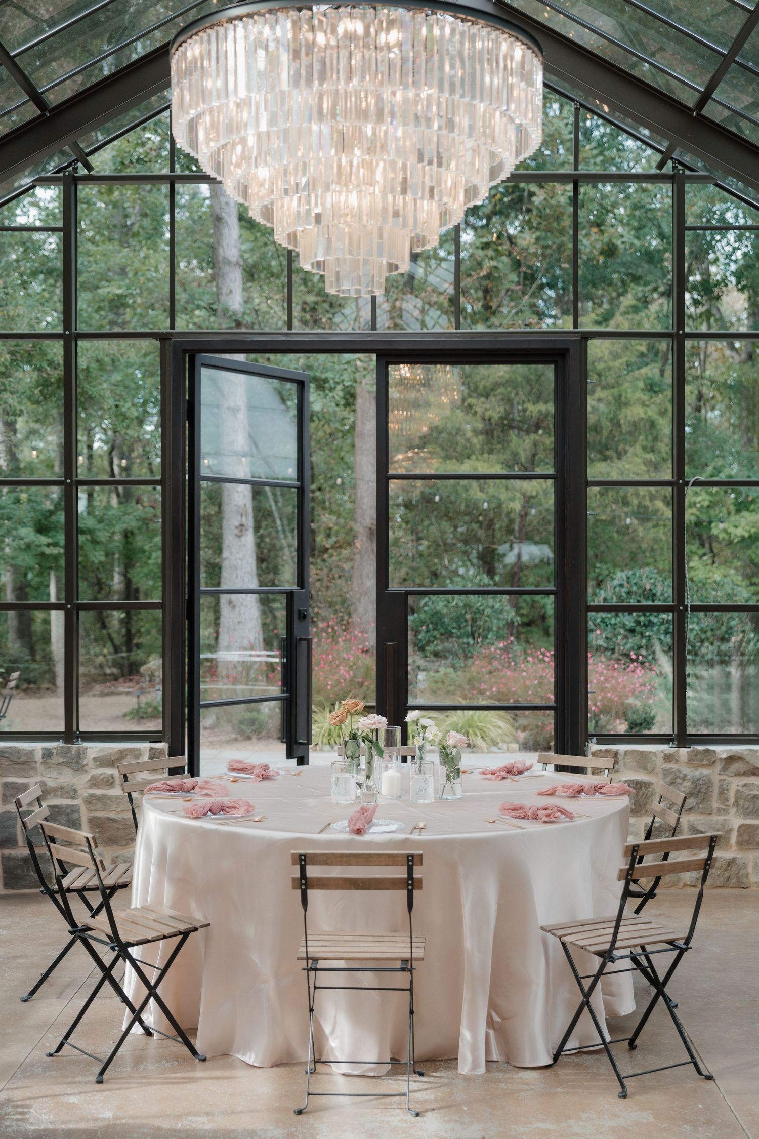 Elegant wedding reception venue with crystal chandelier, floor-to-ceiling windows, and round tables set with white linens.