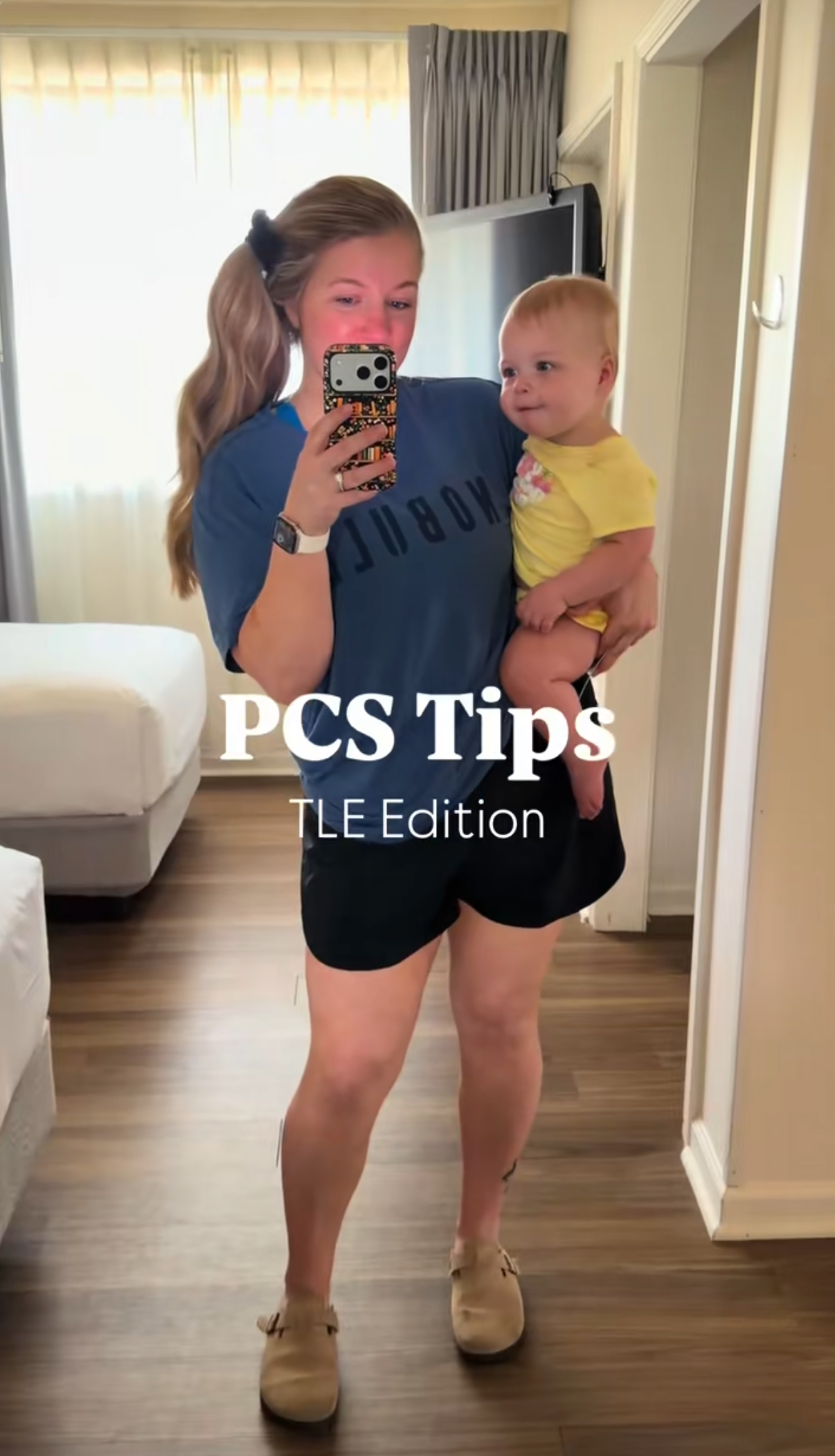Woman holding baby takes mirror selfie in hotel room, text overlay reads PCS Tips TLE Edition for military families.