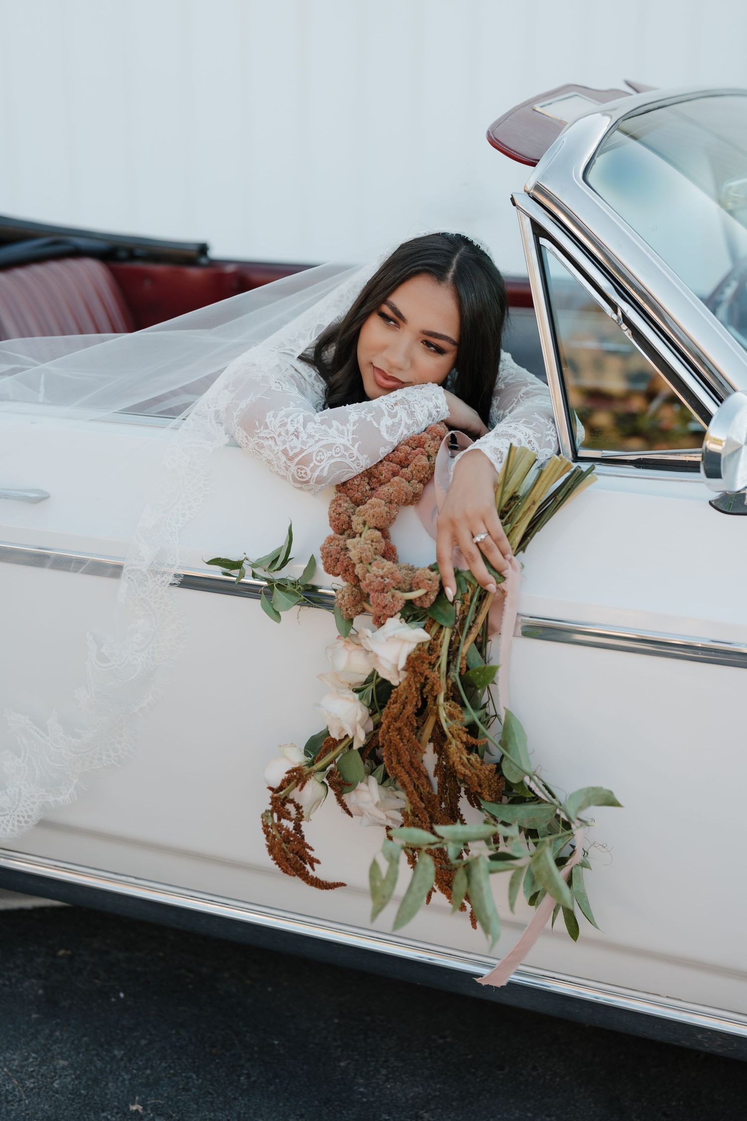 A white vintage car with a floral bouquet draped out the window creates an elegant wedding photo composition.