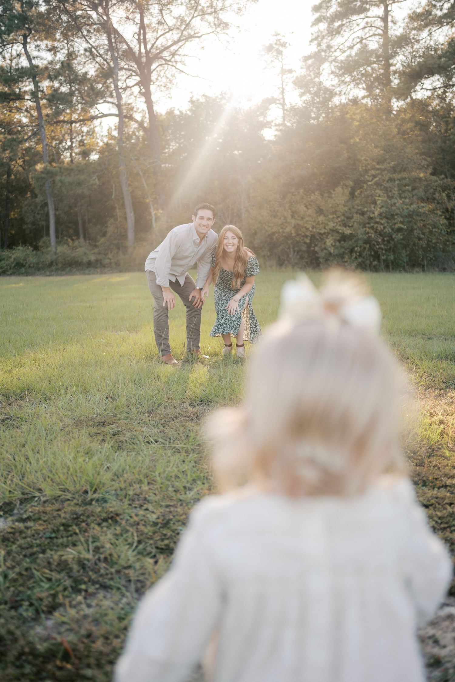 A family enjoys a golden sunset moment together on a grassy field with sunbeams streaming through trees.