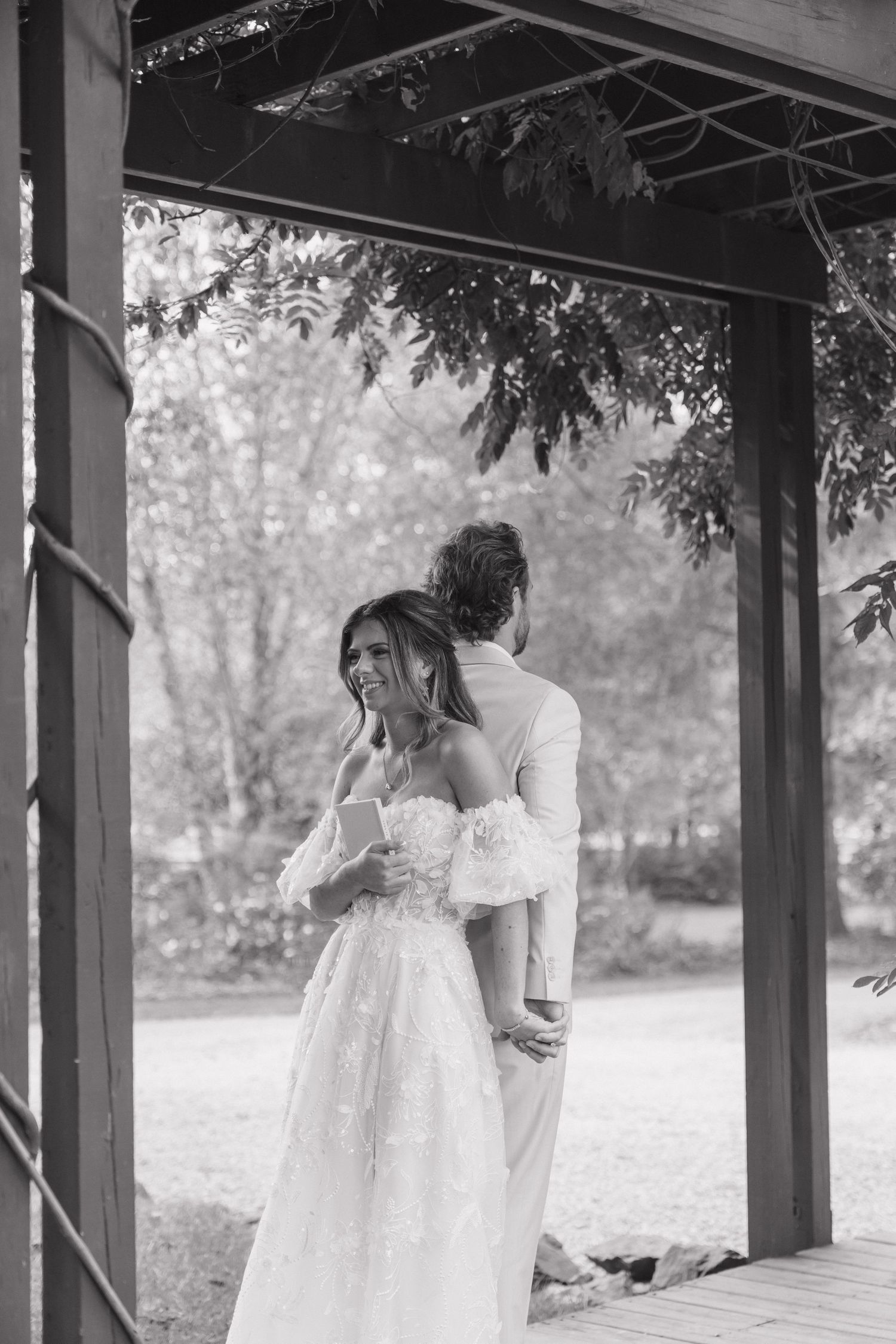 A bride adjusts her shoe while sitting on a rustic wooden porch in a dreamy outdoor setting.