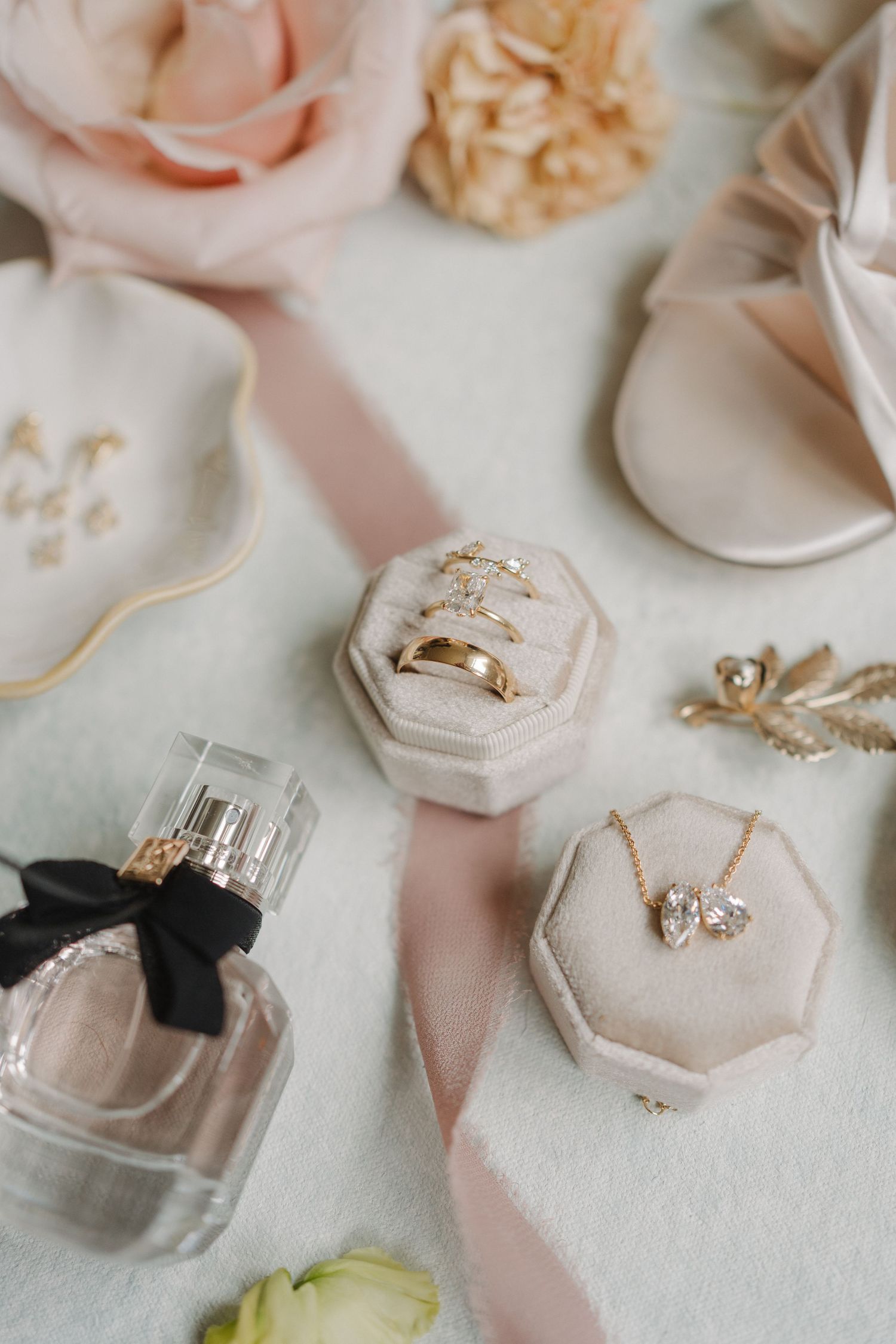 Delicate blush pink velvet ring boxes with gold accents and jewelry displayed on a light surface.