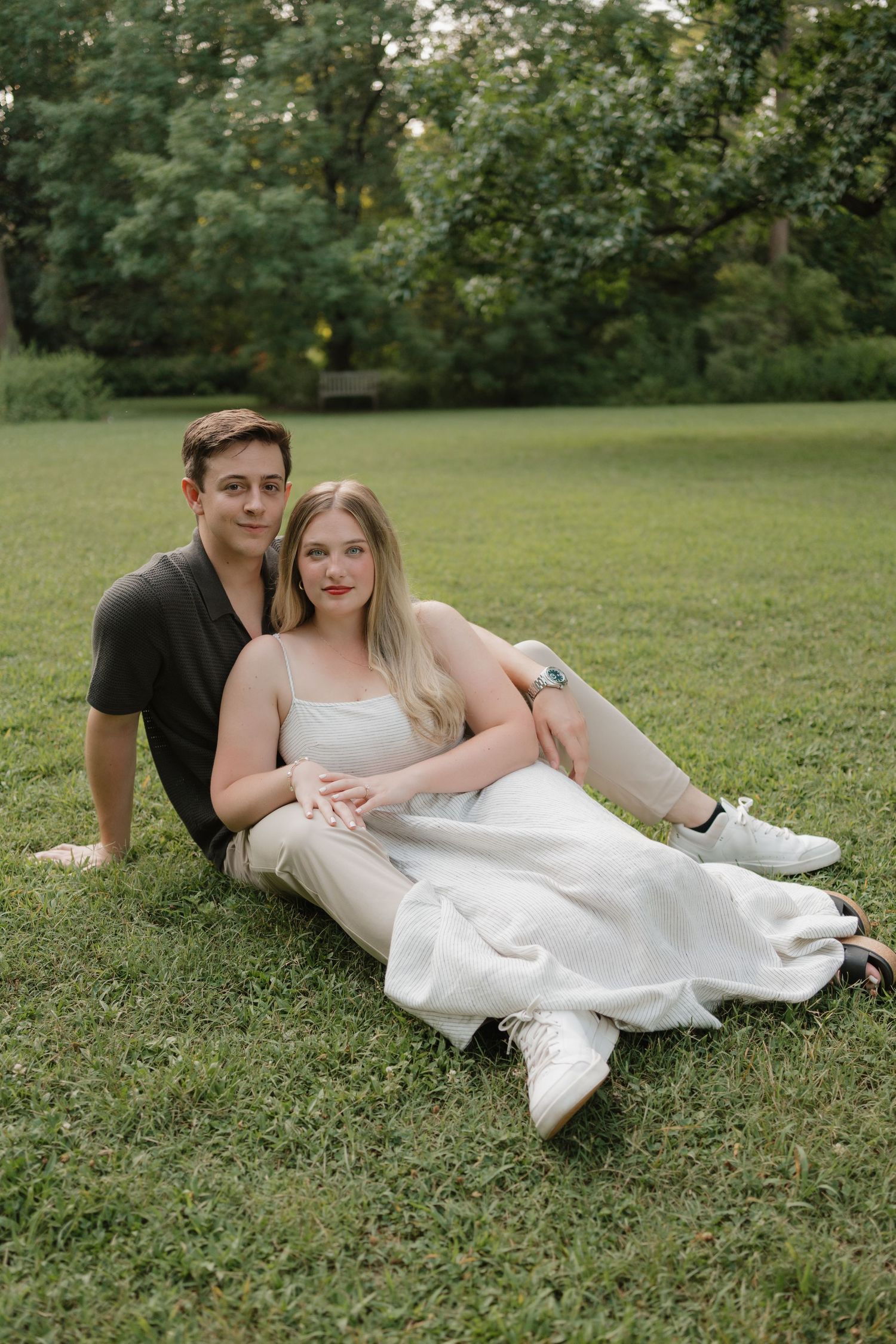 A couple lying together on green grass in romantic wedding attire during an outdoor photo session.
