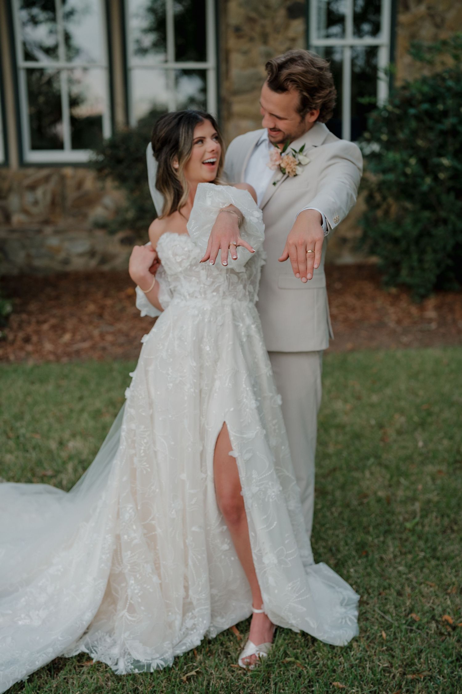 A couple shares a romantic dance moment on a grassy lawn in elegant wedding attire.