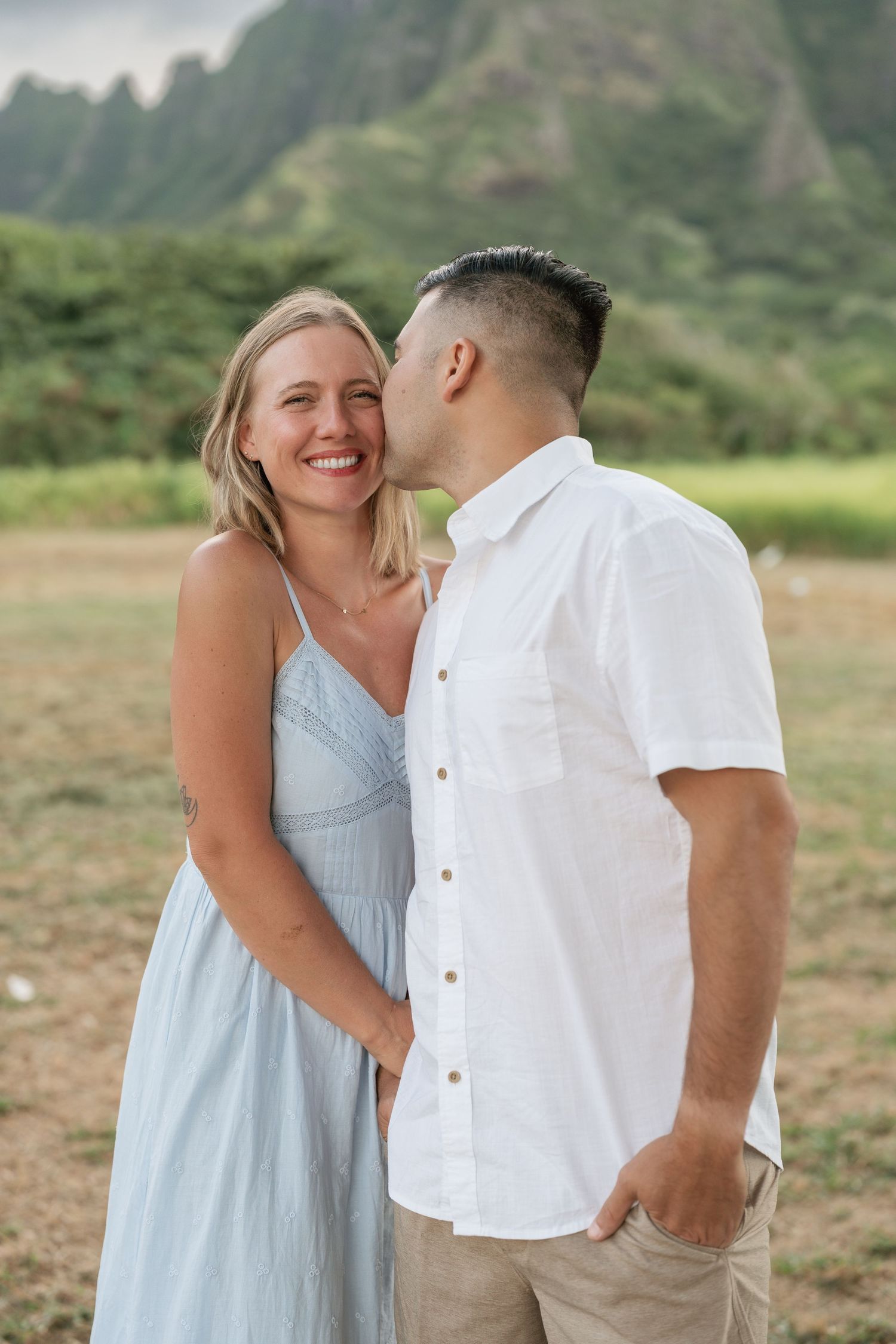 Couple sharing a romantic kiss with lush green mountains in the background in Hawaii.