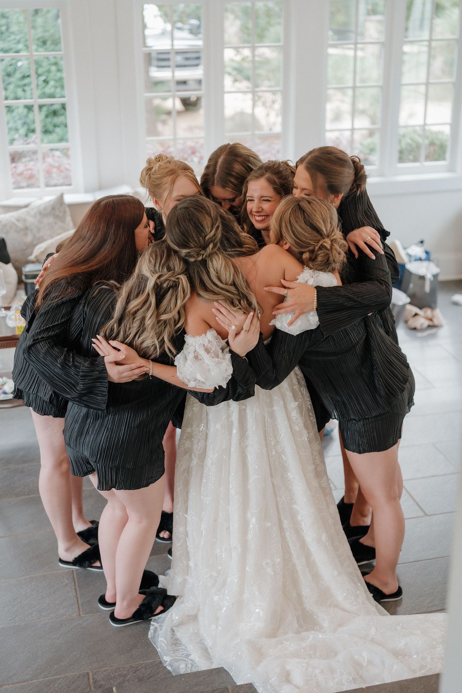 Bridesmaids in black dresses huddle together with the bride in white for a candid group photo.