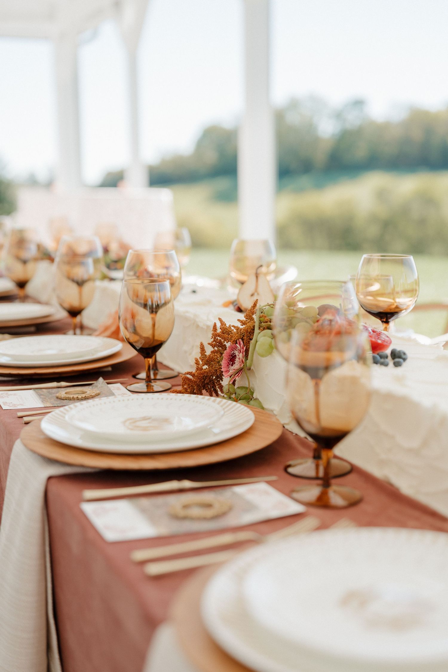 Elegant table setting with dusty rose tablecloth, white plates, wine glasses and floral centerpieces at outdoor venue.