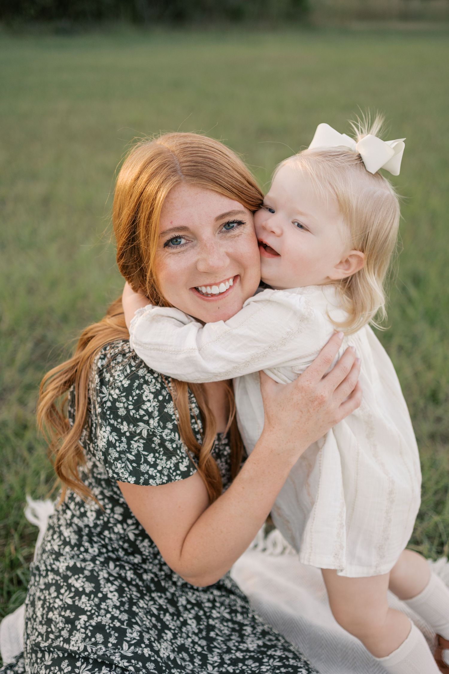 A sweet embrace outdoors shows a floral dress and white outfit against a soft green grassy background.