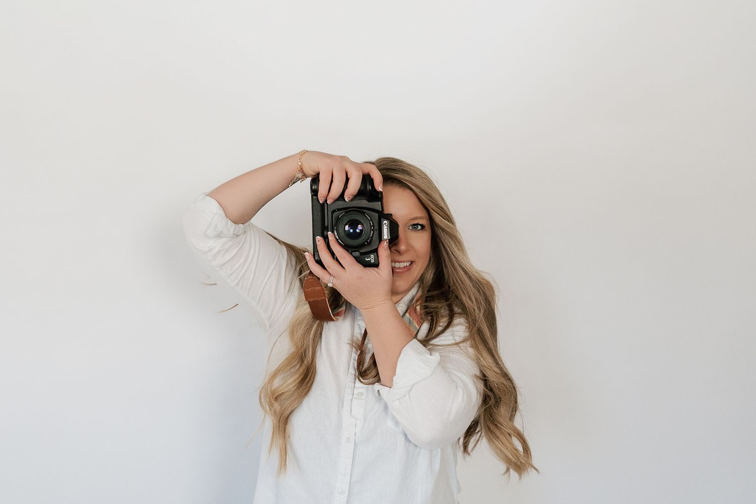 A photographer in a white shirt takes a selfie with a vintage camera against a light background.