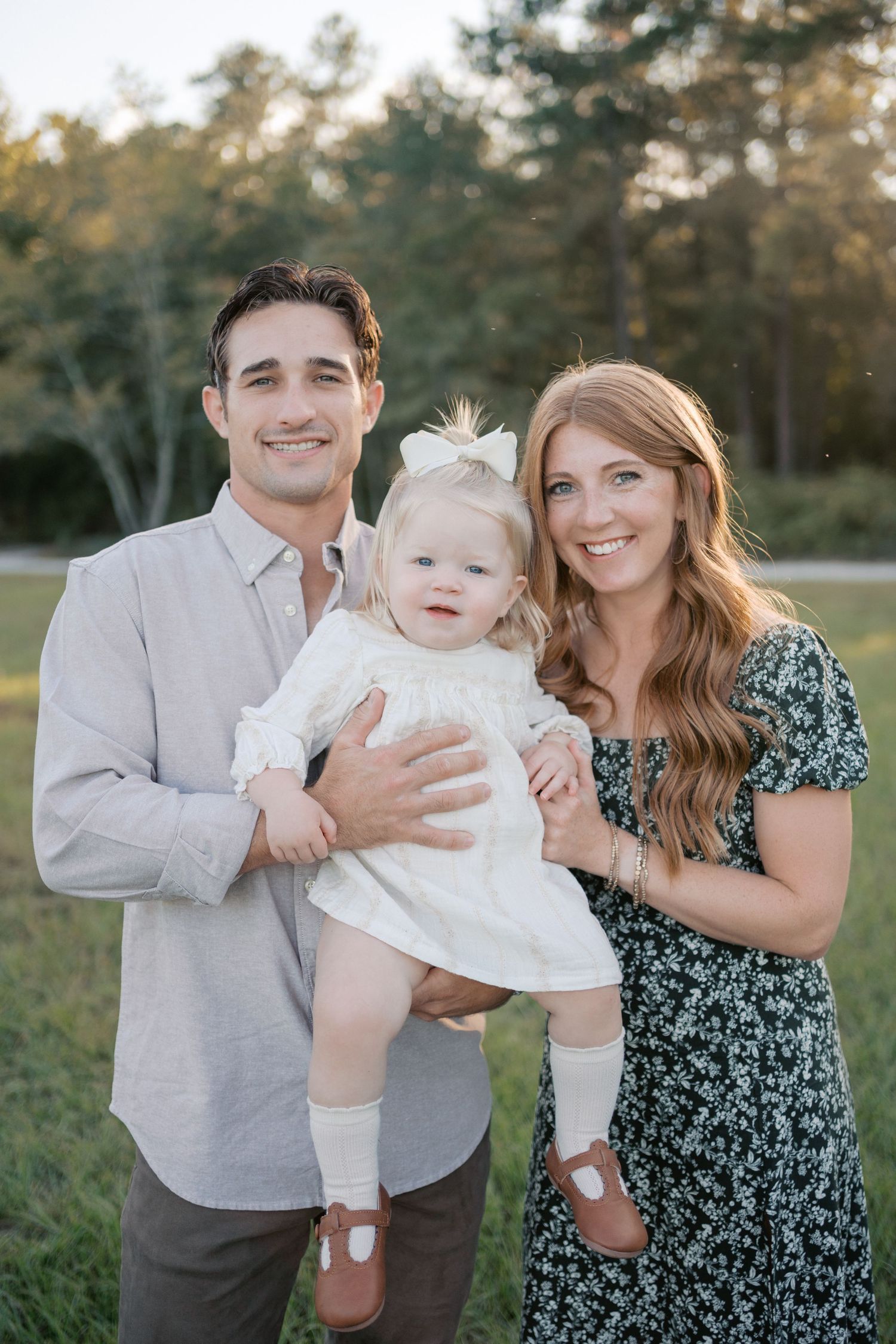 A happy family portrait taken outdoors with beautiful golden sunlight filtering through trees in the background.