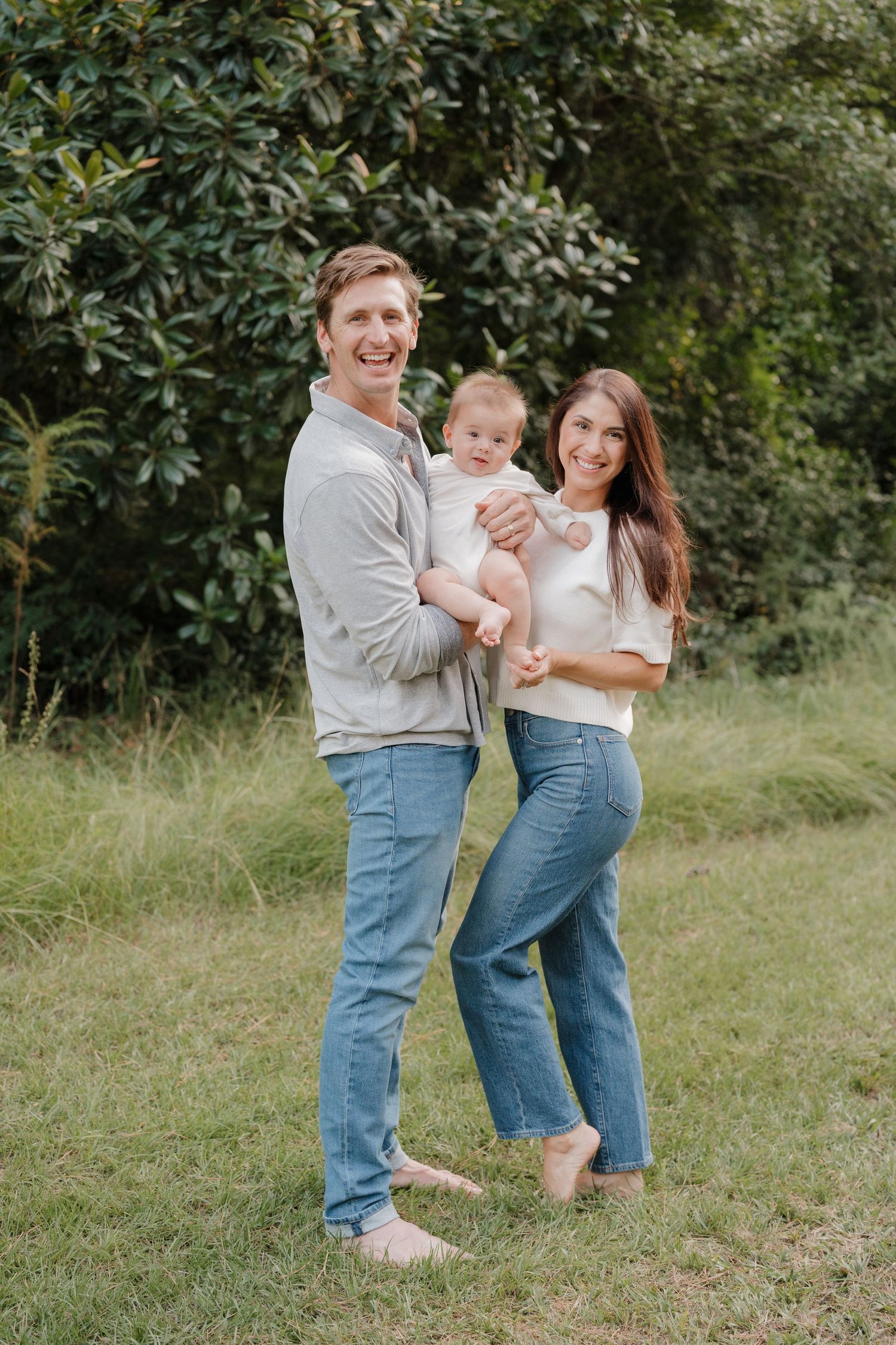 A family in coordinated denim and white outfits shares playful moments together in a grassy outdoor setting.