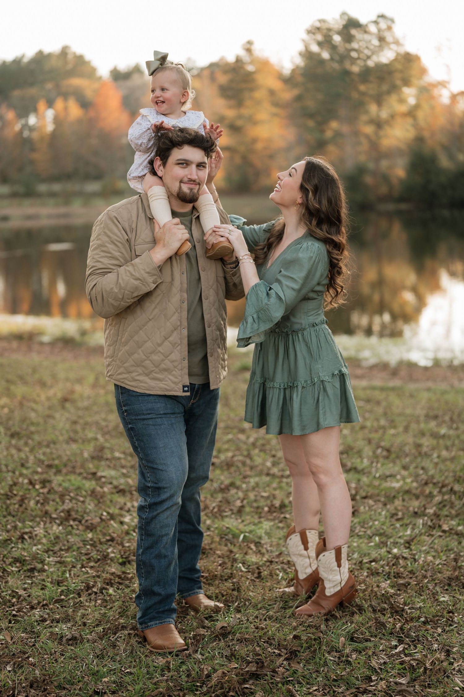 A playful family moment captured outdoors during fall, with brown and green clothing against autumn leaves.