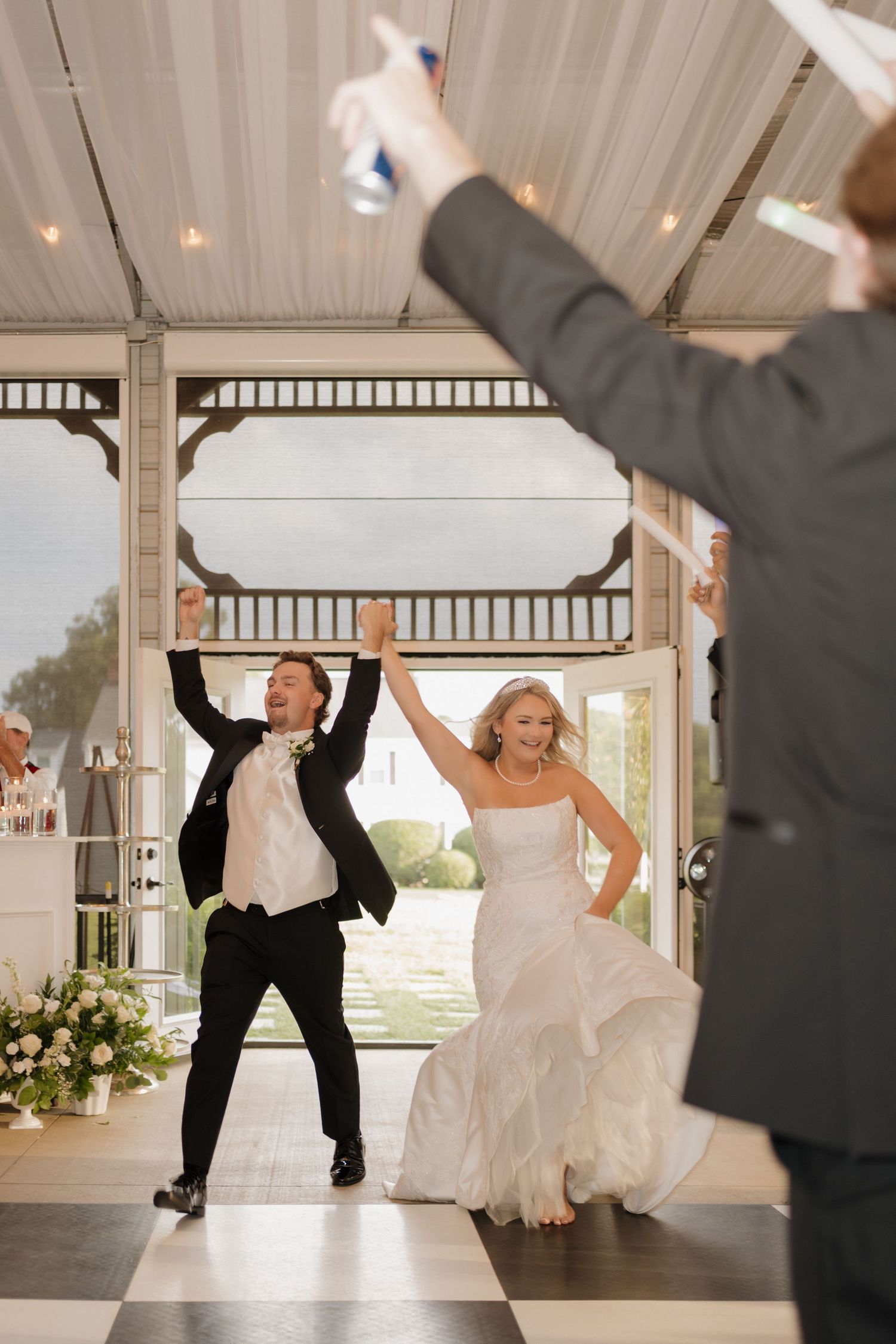Wedding party celebrates on dance floor with coordinated dance moves in elegant indoor venue with white decorations.