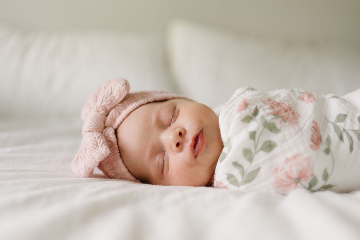 Peaceful newborn baby sleeping in soft white bedding with delicate floral pattern and pink accents.