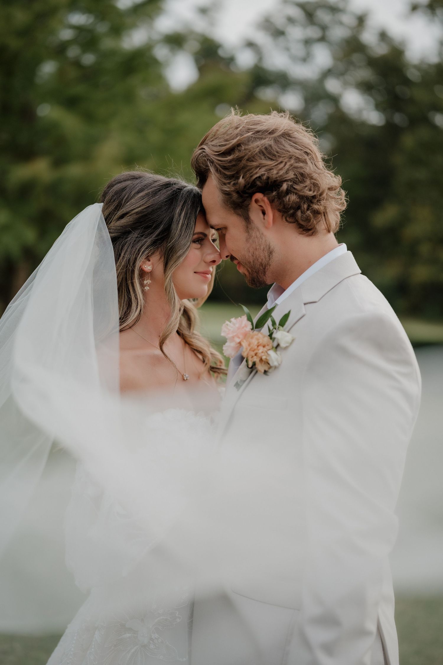 Romantic wedding couple embraces under flowing white veil in outdoor garden setting.