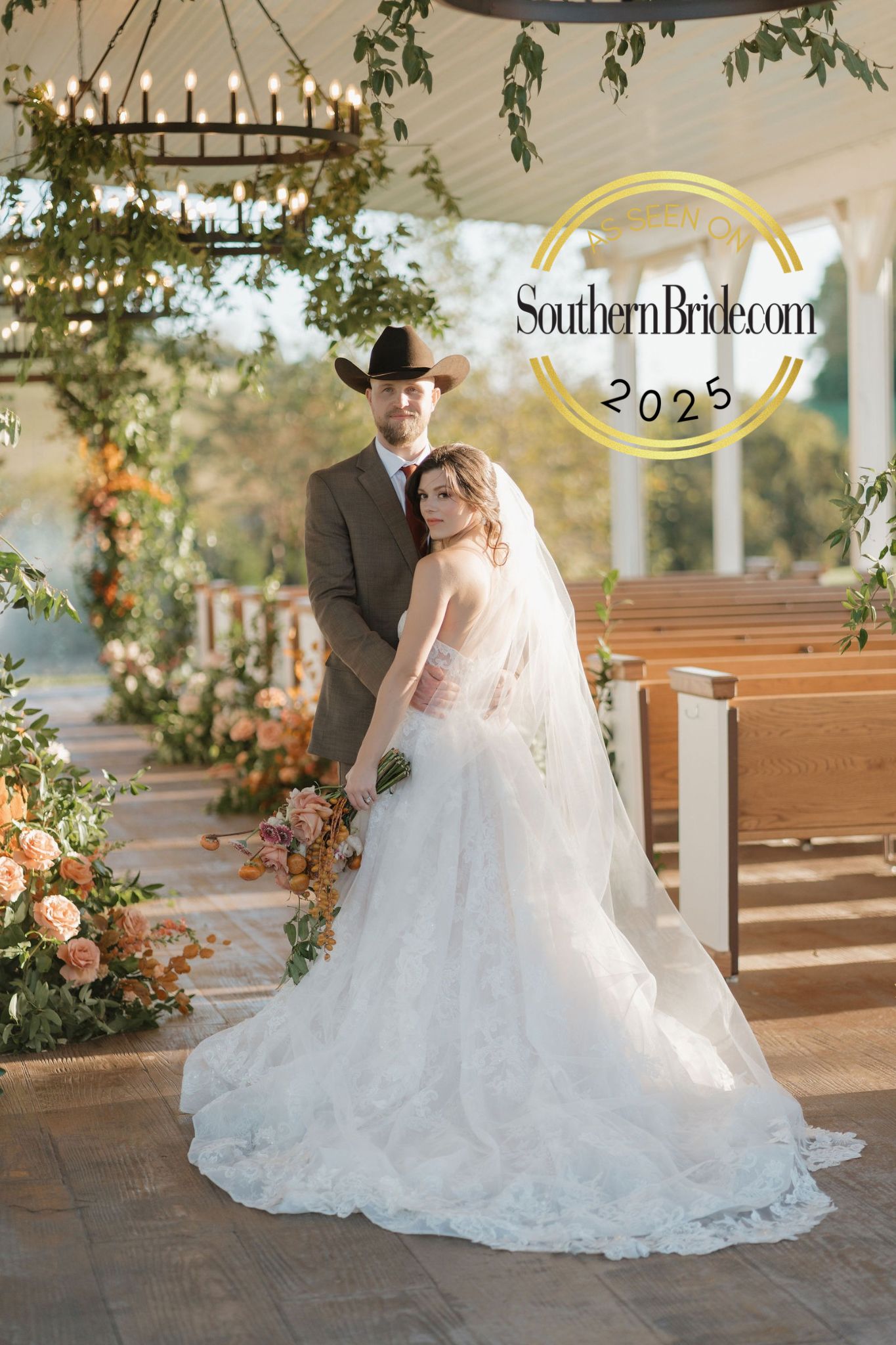 Bride in flowing white lace wedding gown poses in a church aisle decorated with romantic floral arrangements.