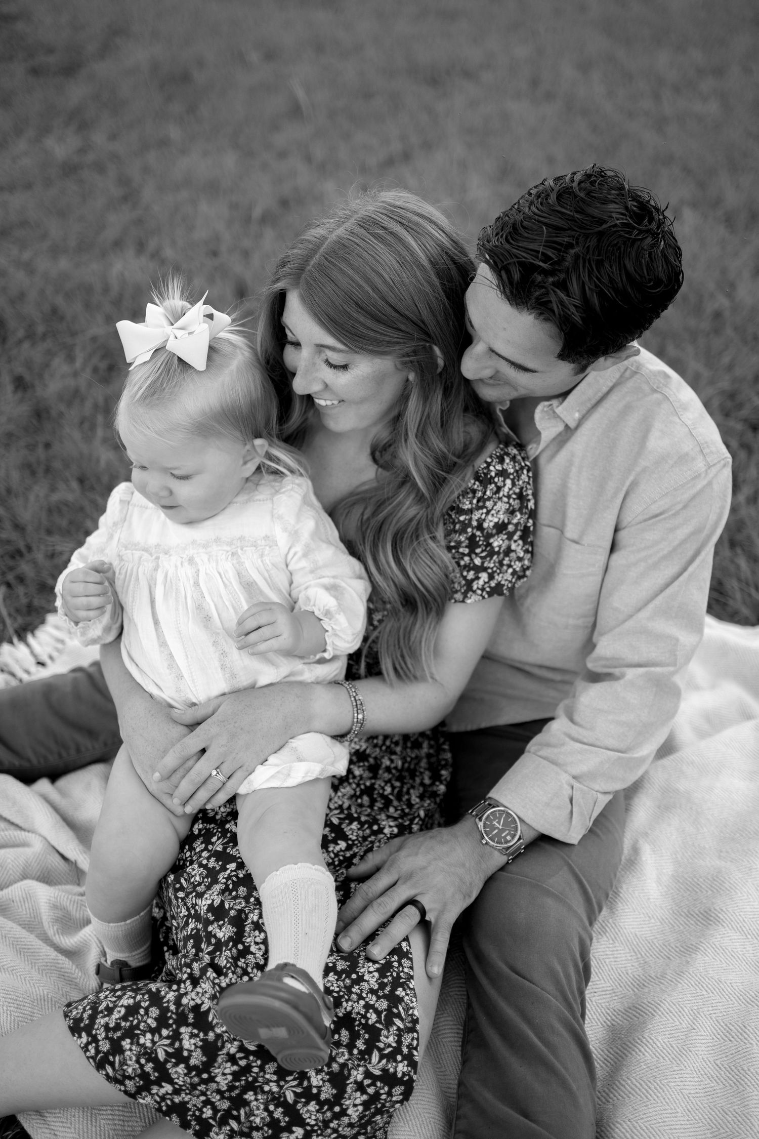 Sweet family moment captured in black and white during outdoor photo session on blanket in grass.