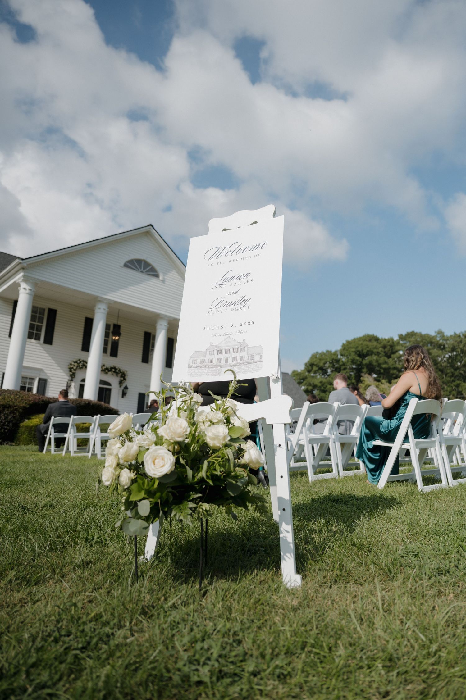 White colonial style house with wedding ceremony setup featuring folding chairs and elegant floral arrangements on the lawn.