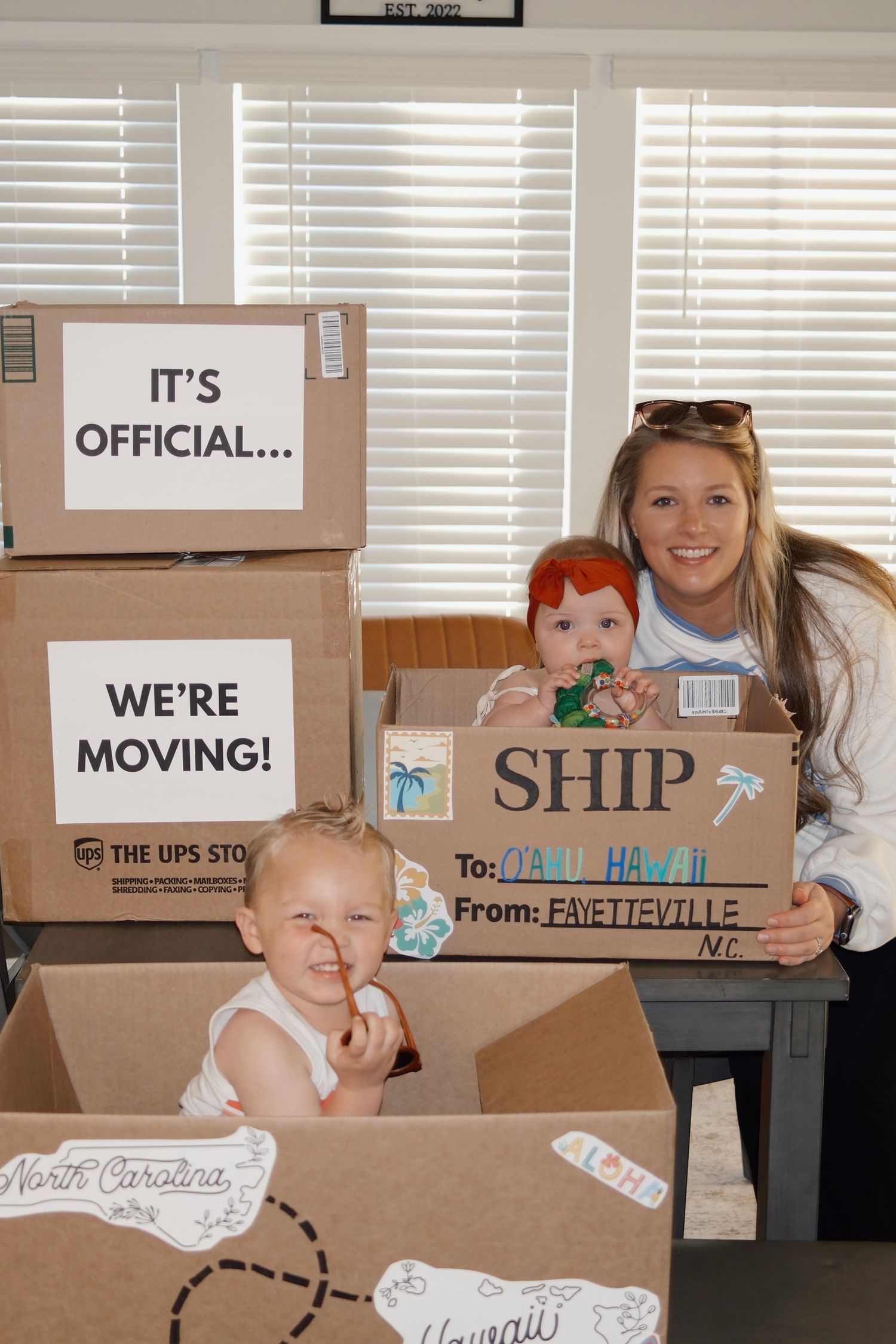 Woman and two babies celebrate moving from Fayetteville NC to Oahu Hawaii with decorated cardboard boxes.