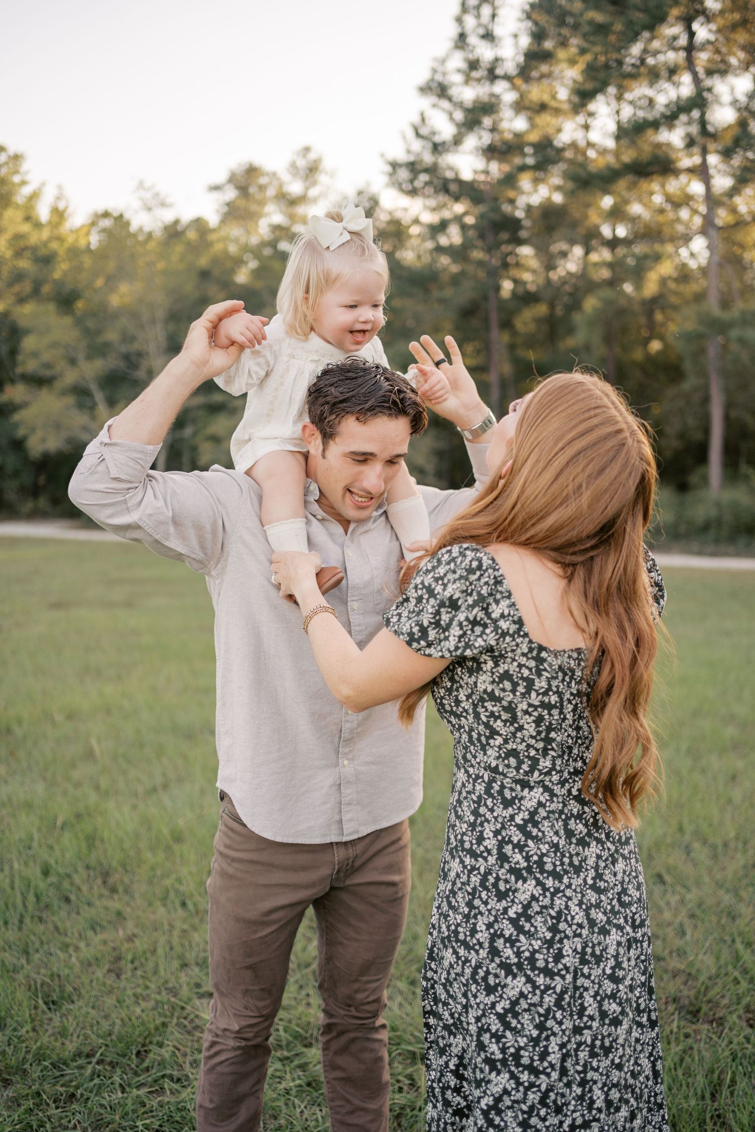 A happy family enjoys playful moments together in a grassy field during sunset, with joyful expressions and natural interactions.