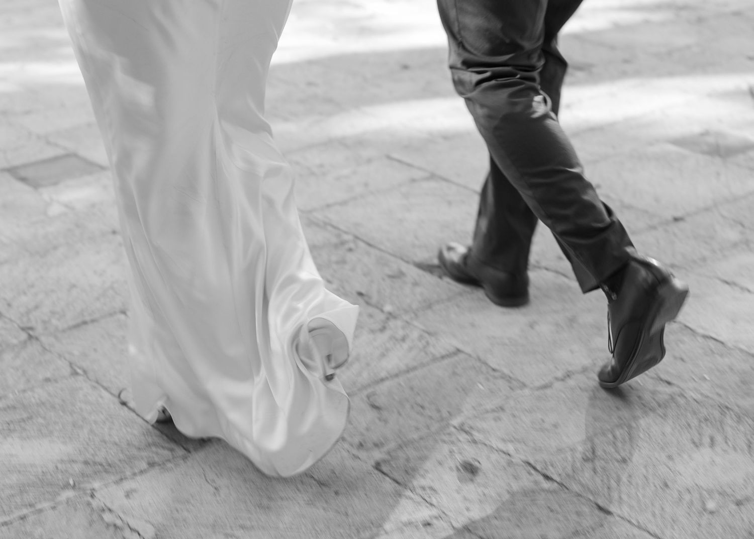Close-up black and white photo of feet dancing on a stone floor during a wedding celebration.