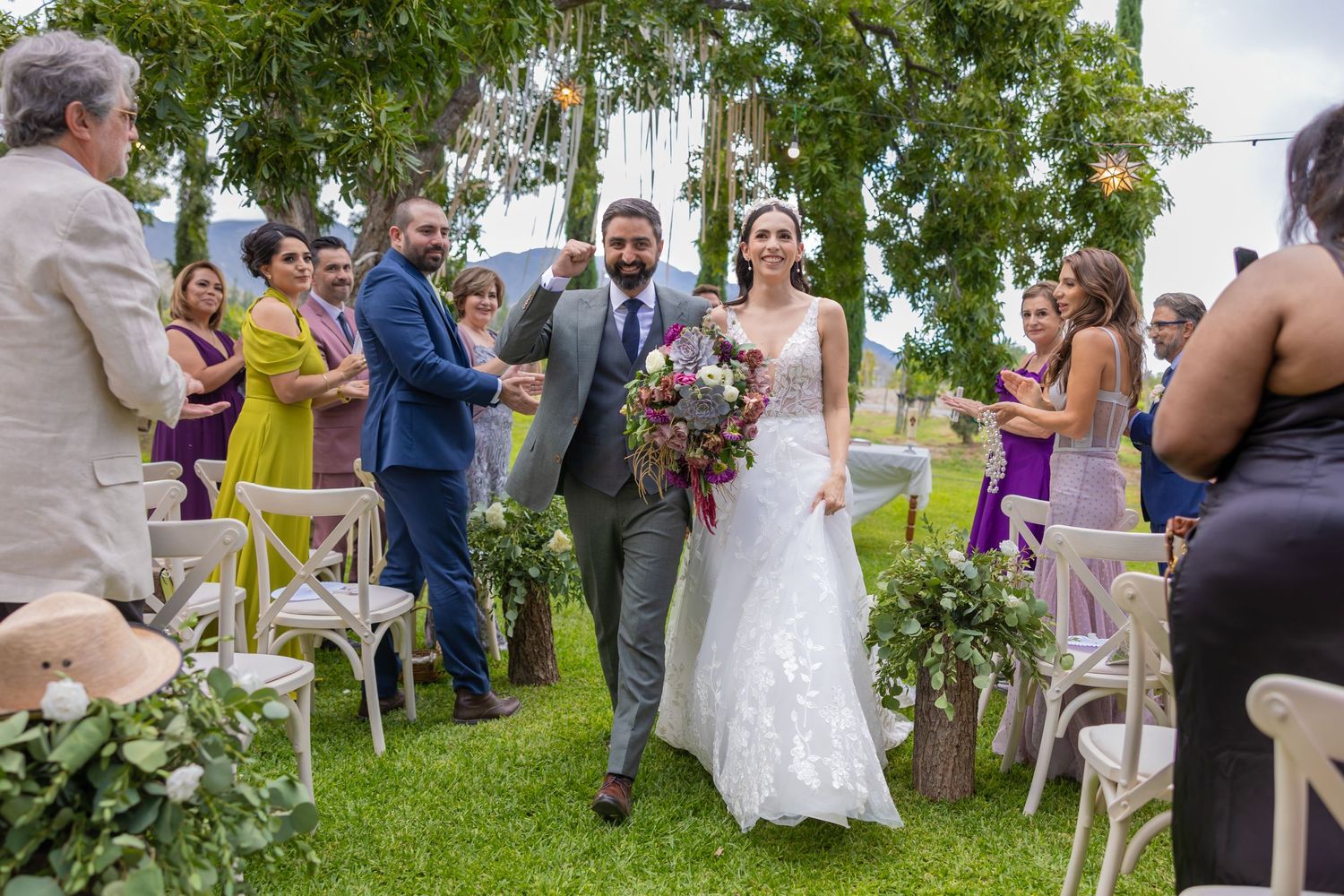 A couple walks down the aisle at an outdoor garden wedding ceremony as guests look on joyfully. Boda en Parras Coahuila fotógrafo