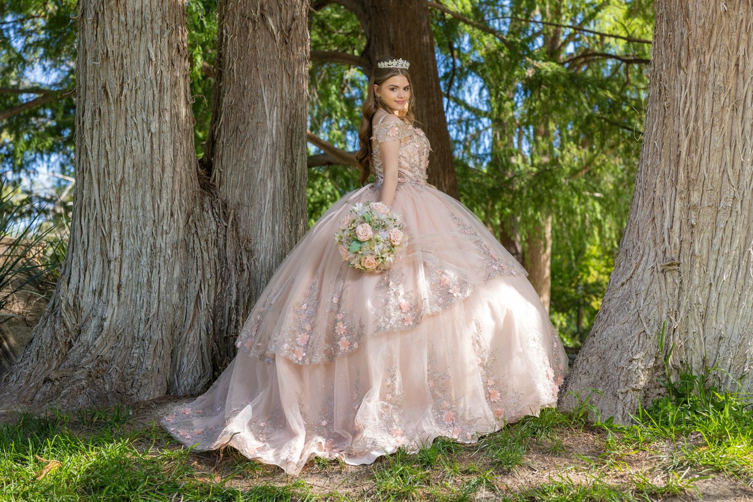 Person in pink princess ballgown posing between large trees in an outdoor garden setting. Evento en Parras Coahuila , Fotógrafo Rulo