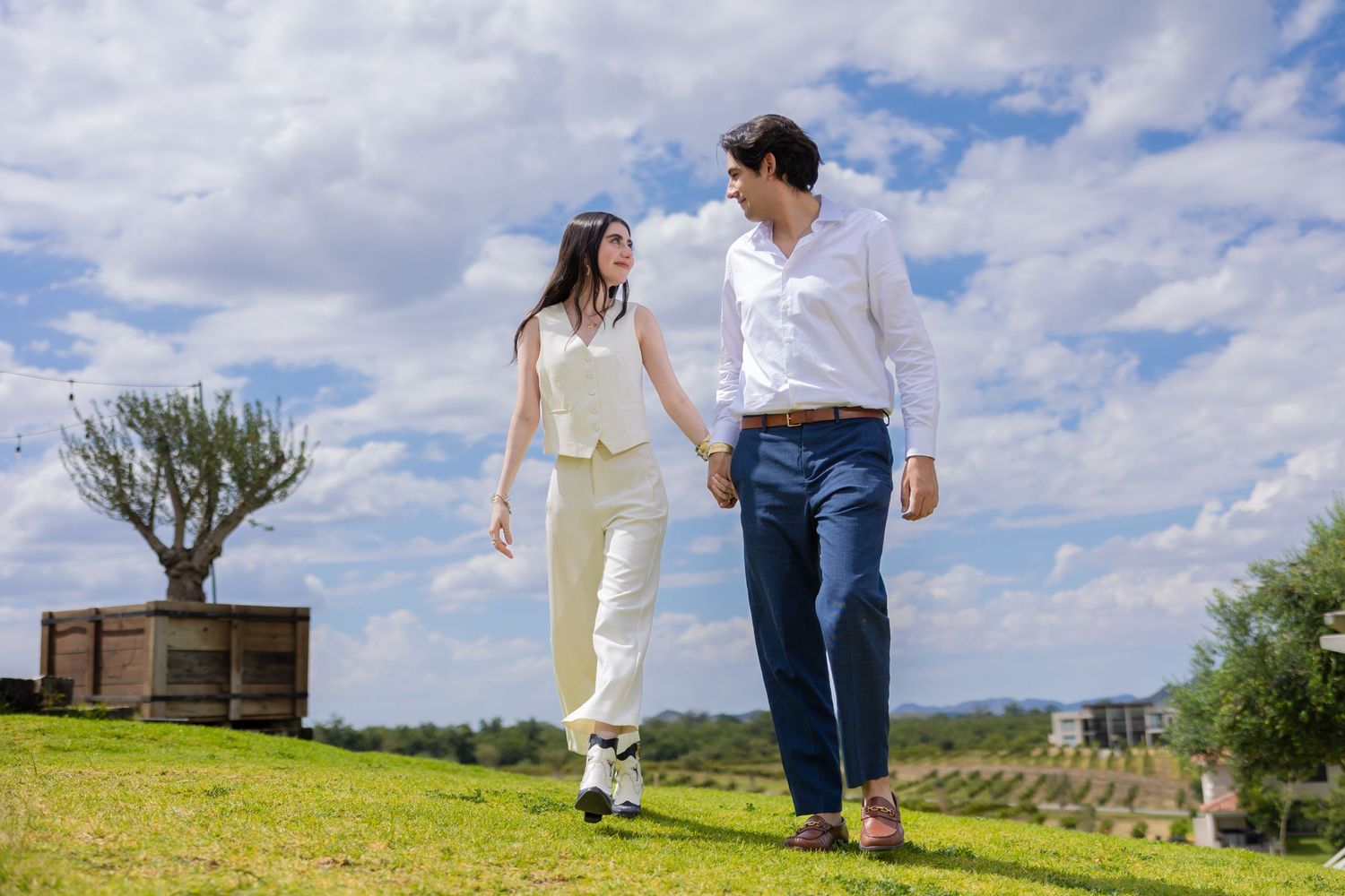 Couple walking together on grassy hilltop under cloudy blue sky. Propuesta de matrimonio Parras, Fotografo