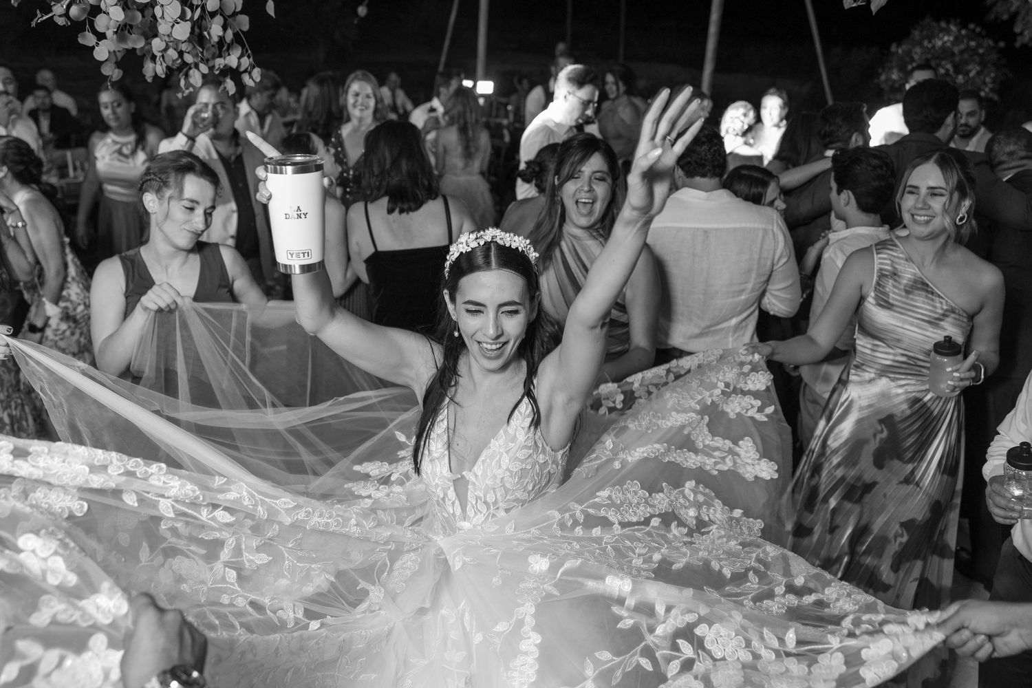 Black and white photo of bride dancing with flowing dress surrounded by celebrating guests. Boda en Parras Coahuila fotógrafo