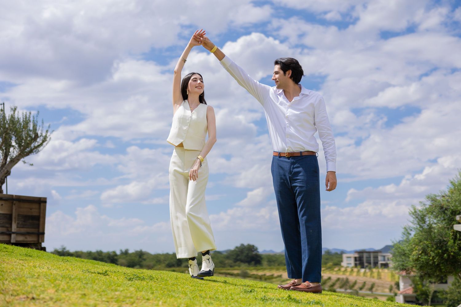 A couple dances together on a grassy hillside with blue skies and white clouds in the background. Propuesta de matrimonio Parras, Fotografo