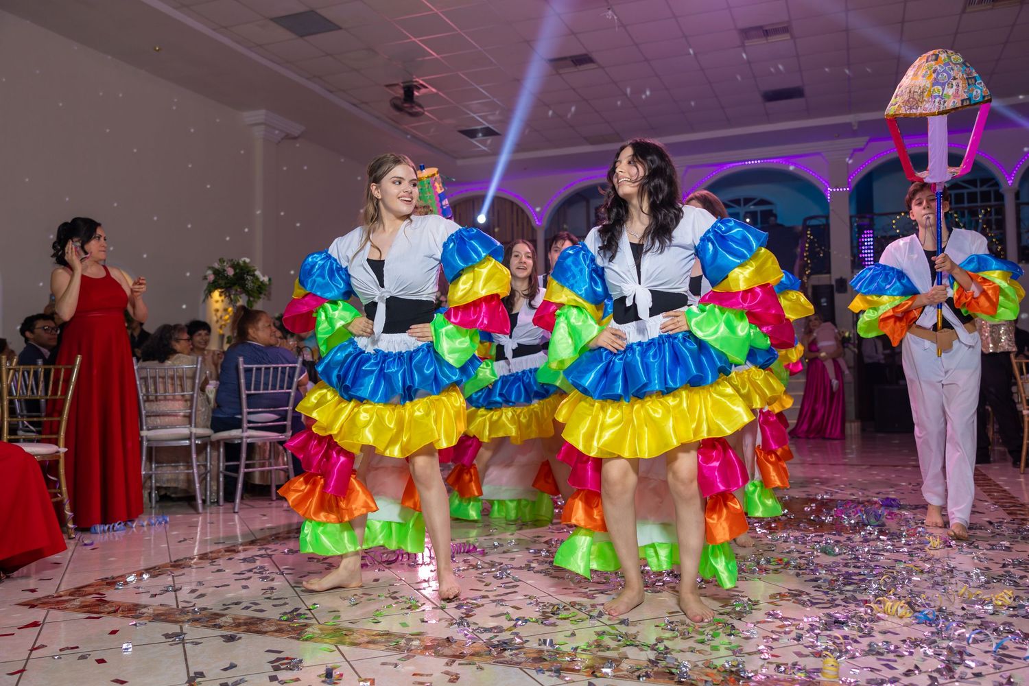 Dancers in vibrant carnival costumes perform in a purple-lit indoor celebration space. Evento en Parras Coahuila , Fotógrafo Rulo