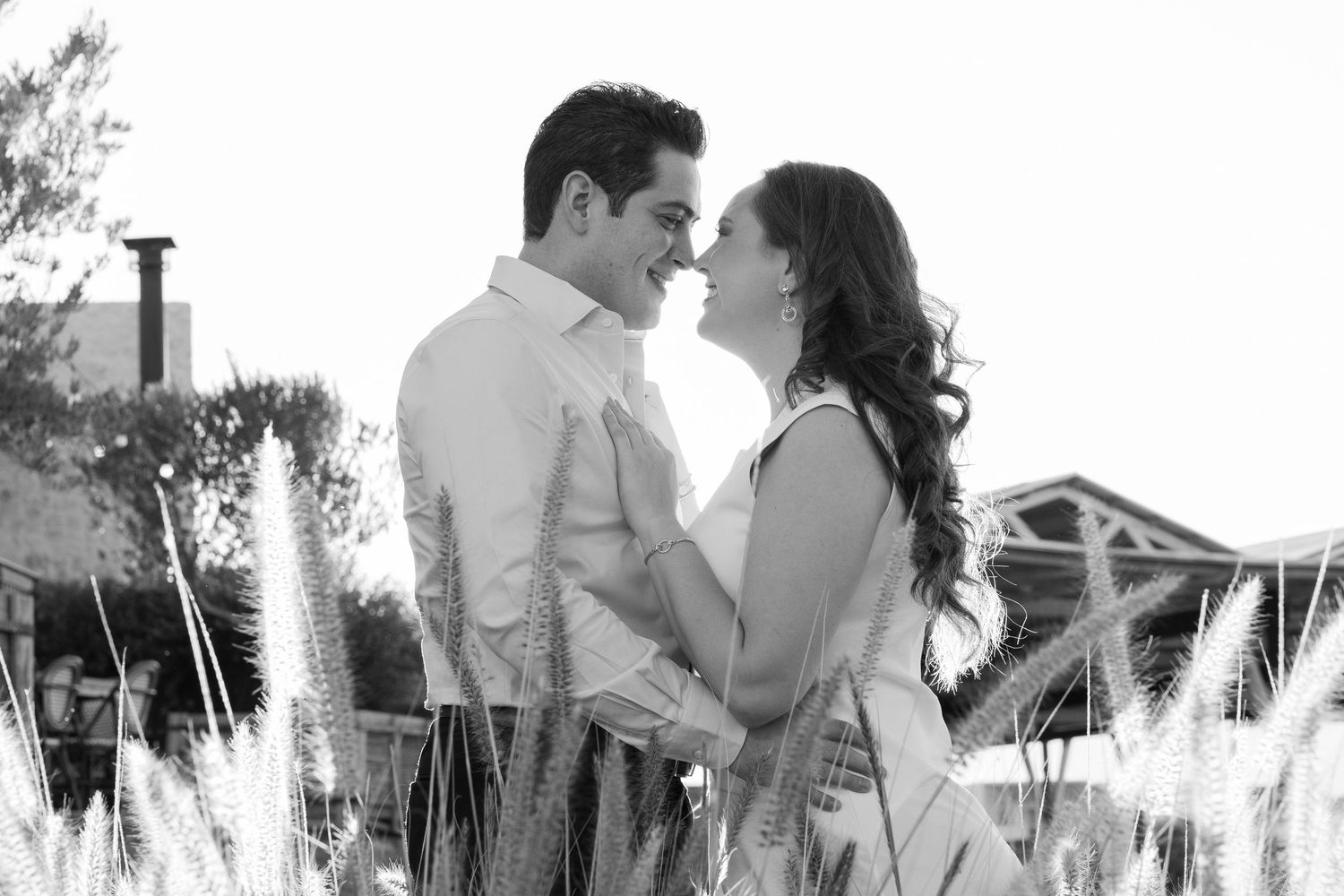 A romantic couple embraces on a sunny day in a scenic outdoor setting with palm trees in the background.