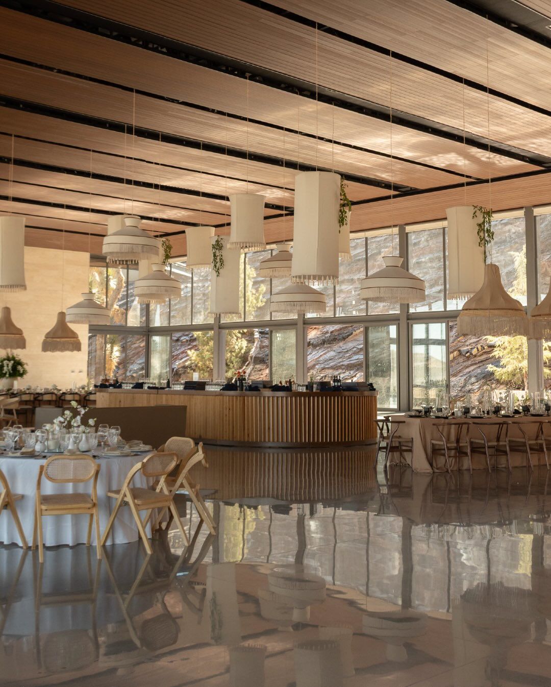 Modern banquet hall interior with wooden ceiling beams, pendant lights and elegant table settings for an upscale event.