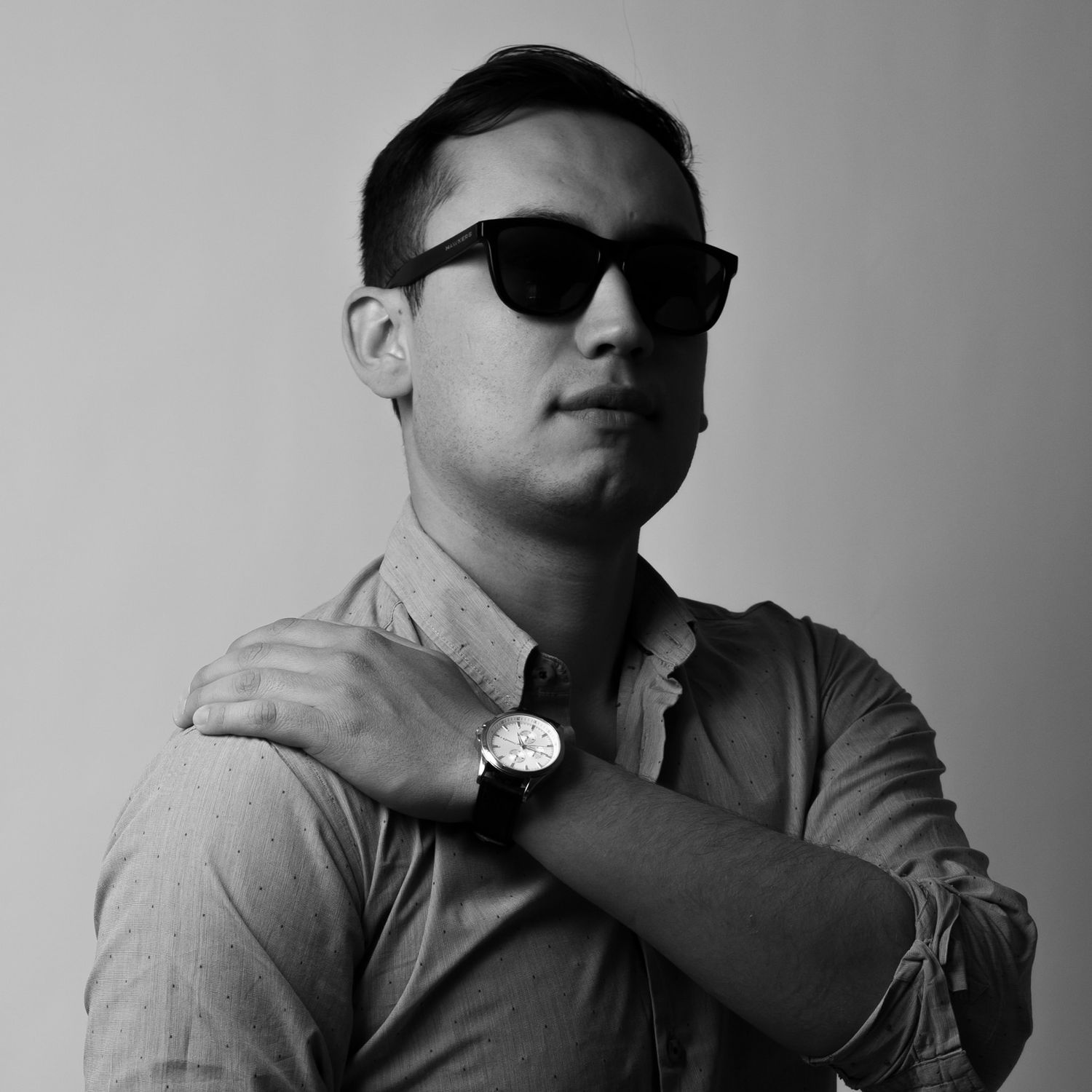 A black and white portrait of a person wearing sunglasses and a watch against a plain background.