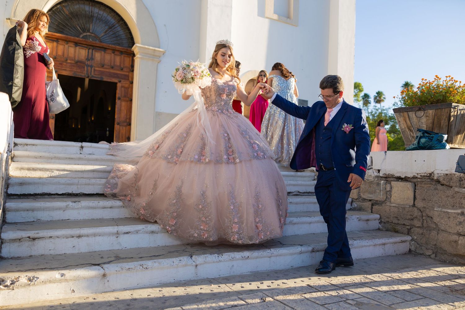 Celebrant in pink ball gown descends church steps with escort in formal attire. Evento en Parras Coahuila , Fotógrafo Rulo