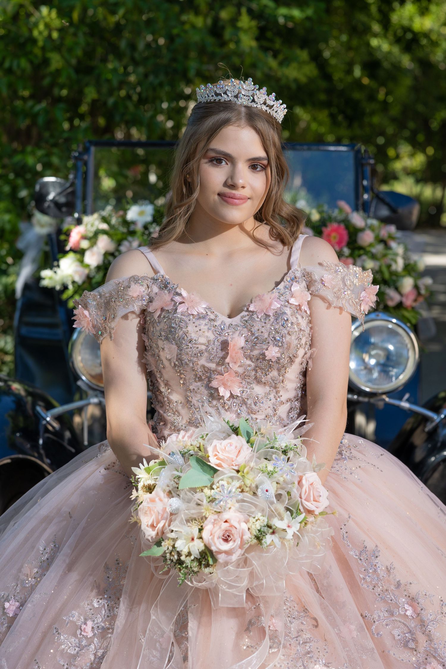 Person in blush pink ballgown with tiara holds floral bouquet in outdoor setting. Evento en Parras Coahuila , Fotógrafo Rulo