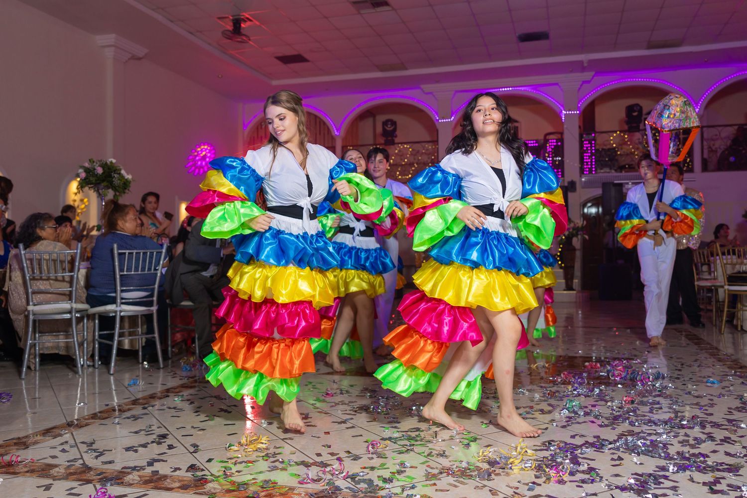 Performers in matching rainbow ruffled dresses dance during an indoor celebration. Evento en Parras Coahuila , Fotógrafo Rulo