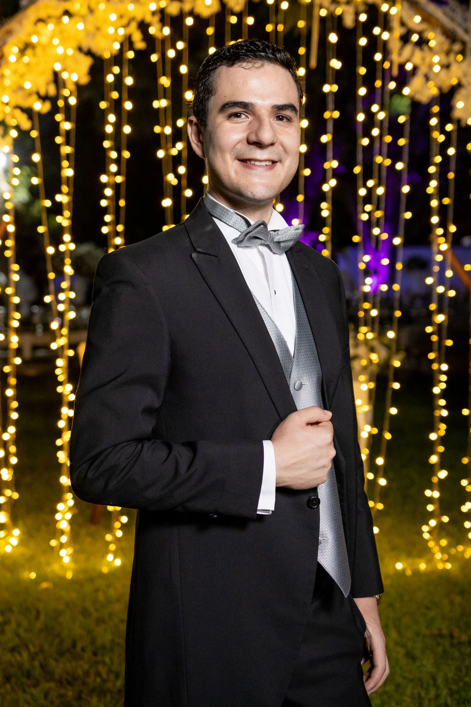 Classic groom portrait against a backdrop of twinkling golden lights in formal black tuxedo. Boda en Parras Coahuila, Fotógrafo de bodas